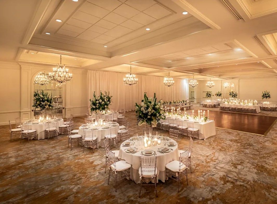 Elegant ballroom with crystal chandeliers, white round tables, and floral centerpieces set for a formal event.