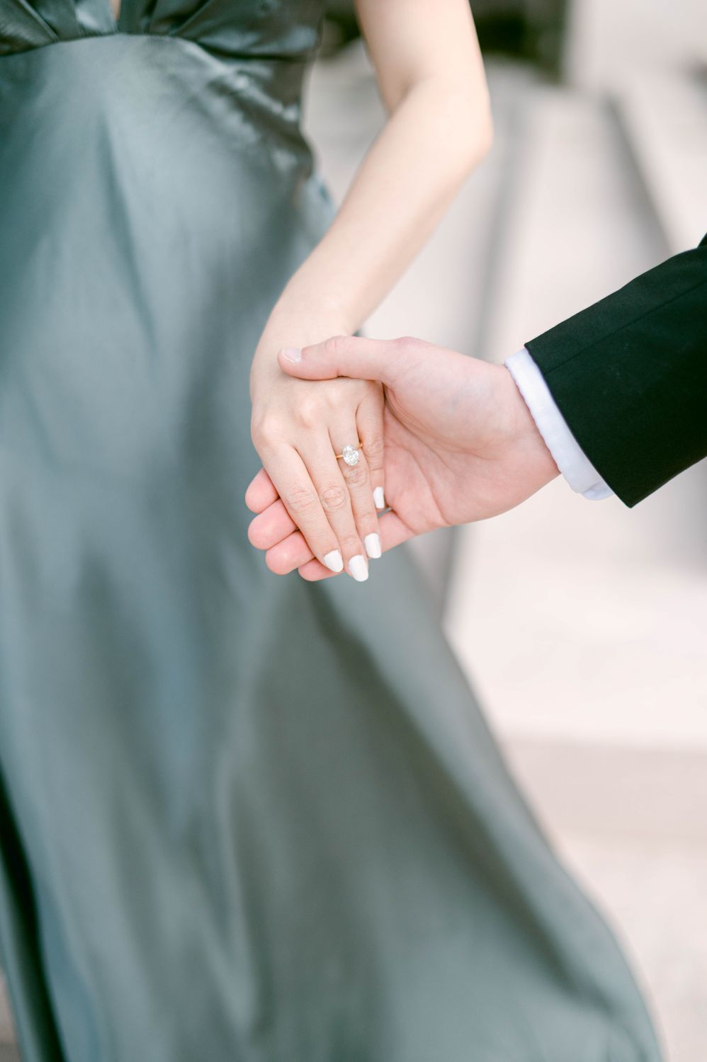 Close-up photo of newlywed couple holding hands showing wedding rings and formal attire.