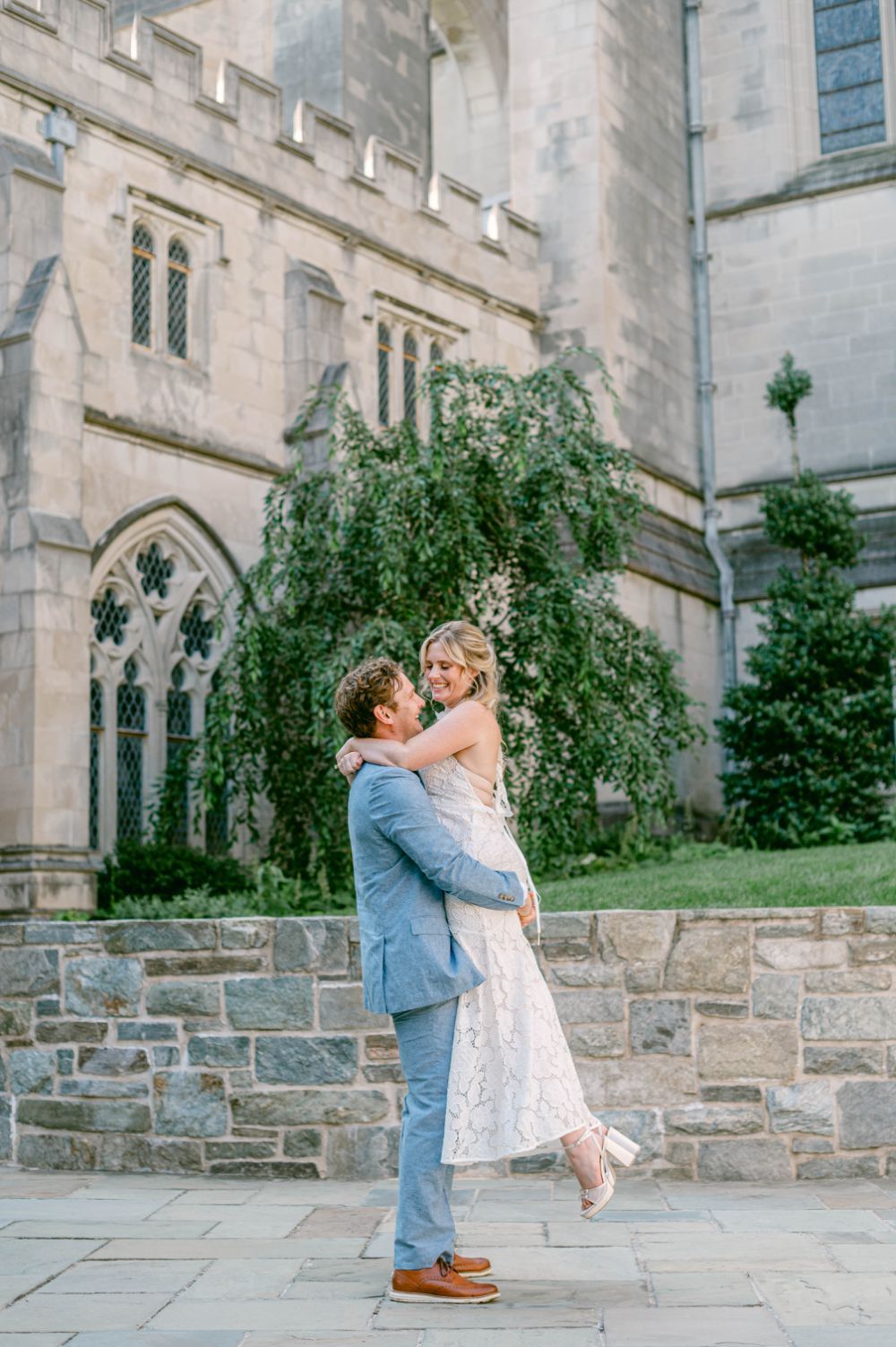 A couple shares a romantic embrace outside a gothic stone church with ornate architecture and climbing vines.