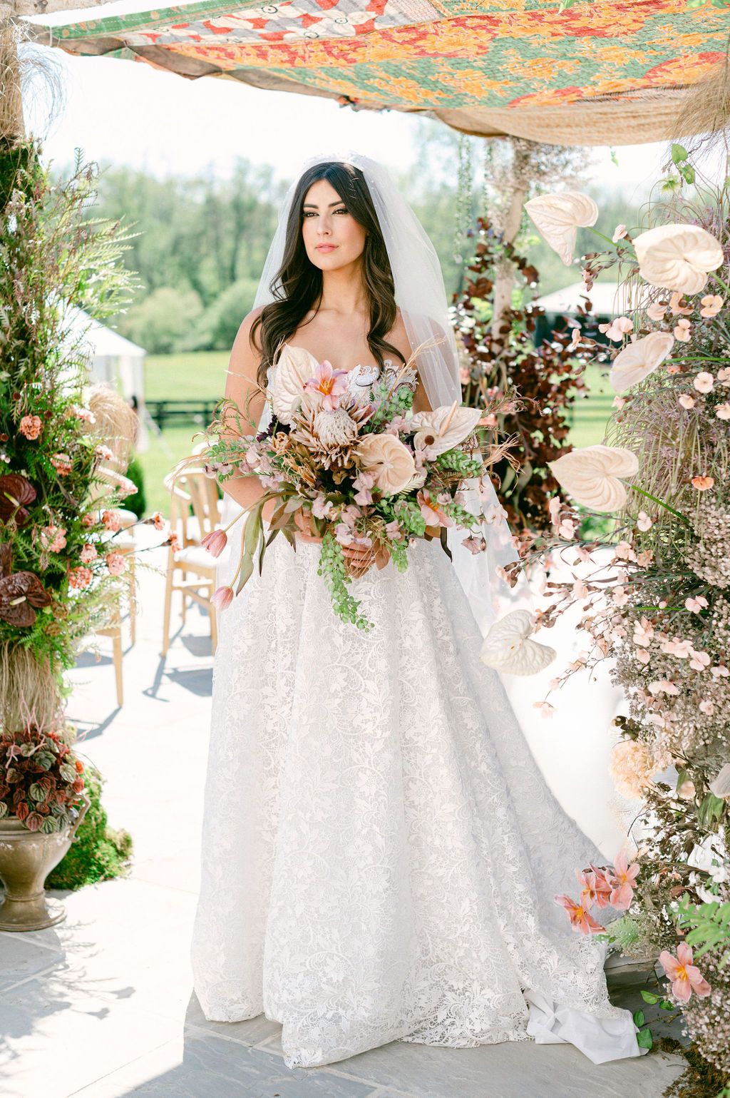 A romantic outdoor wedding scene featuring a white lace ballgown with floral arrangements and draped fabric decor.