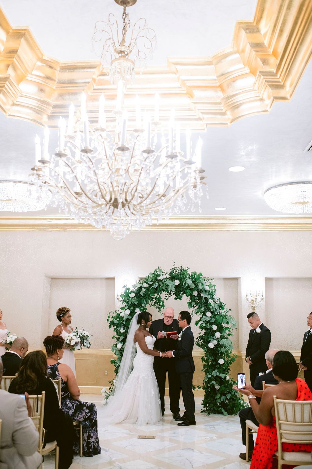 Elegant wedding ceremony sequence in white ballroom with crystal chandeliers and floral arch.