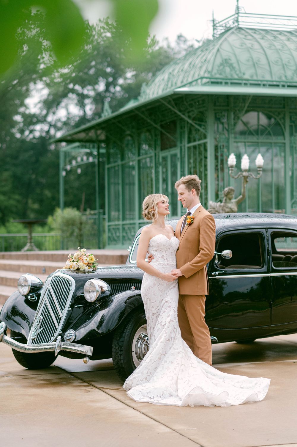 A classic 1930s black Citroën car parked by an ornate Victorian-style glass gazebo during a wedding celebration.