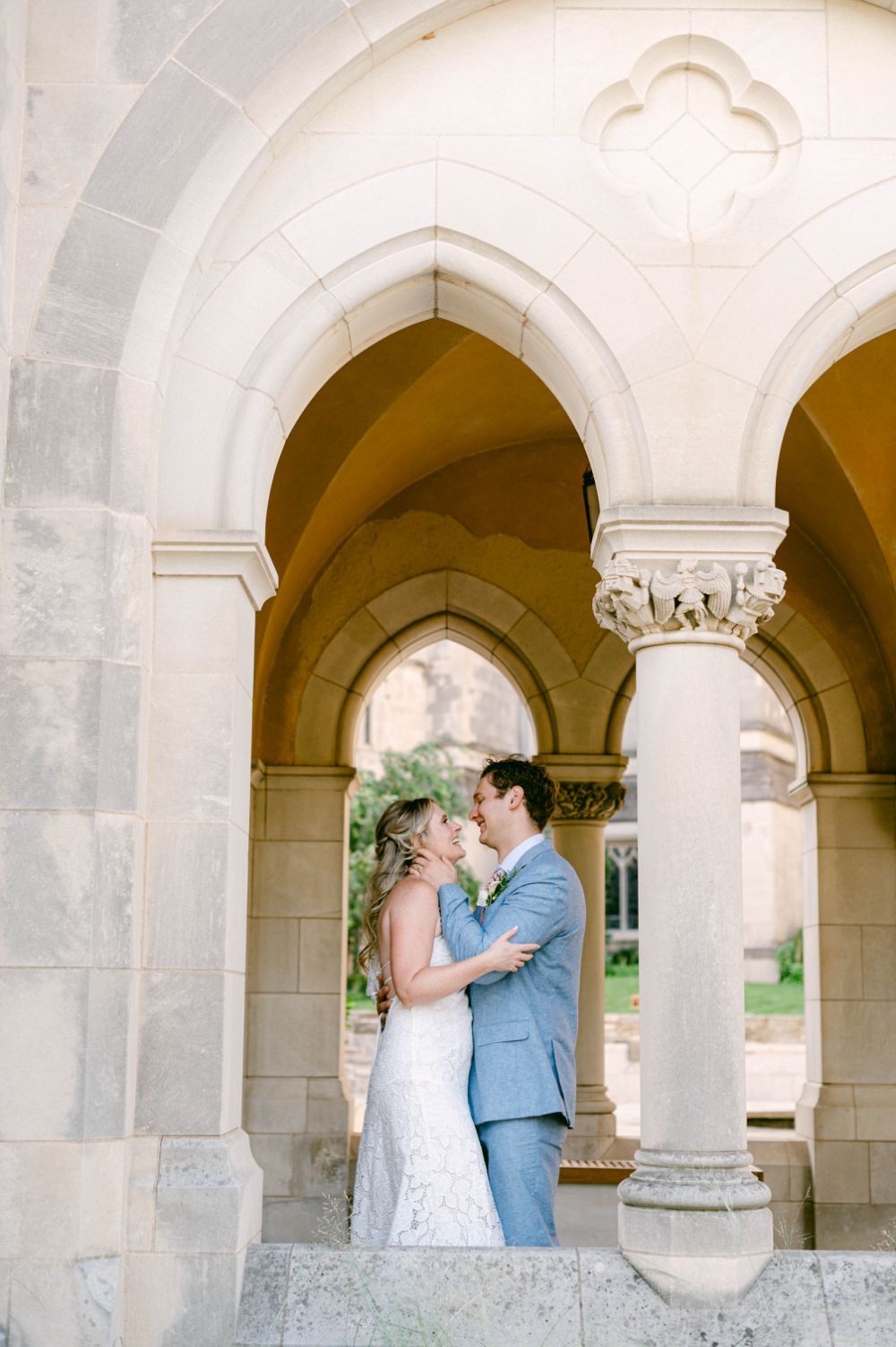A romantic archway photo featuring a couple embracing in elegant wedding attire at a gothic architectural setting.