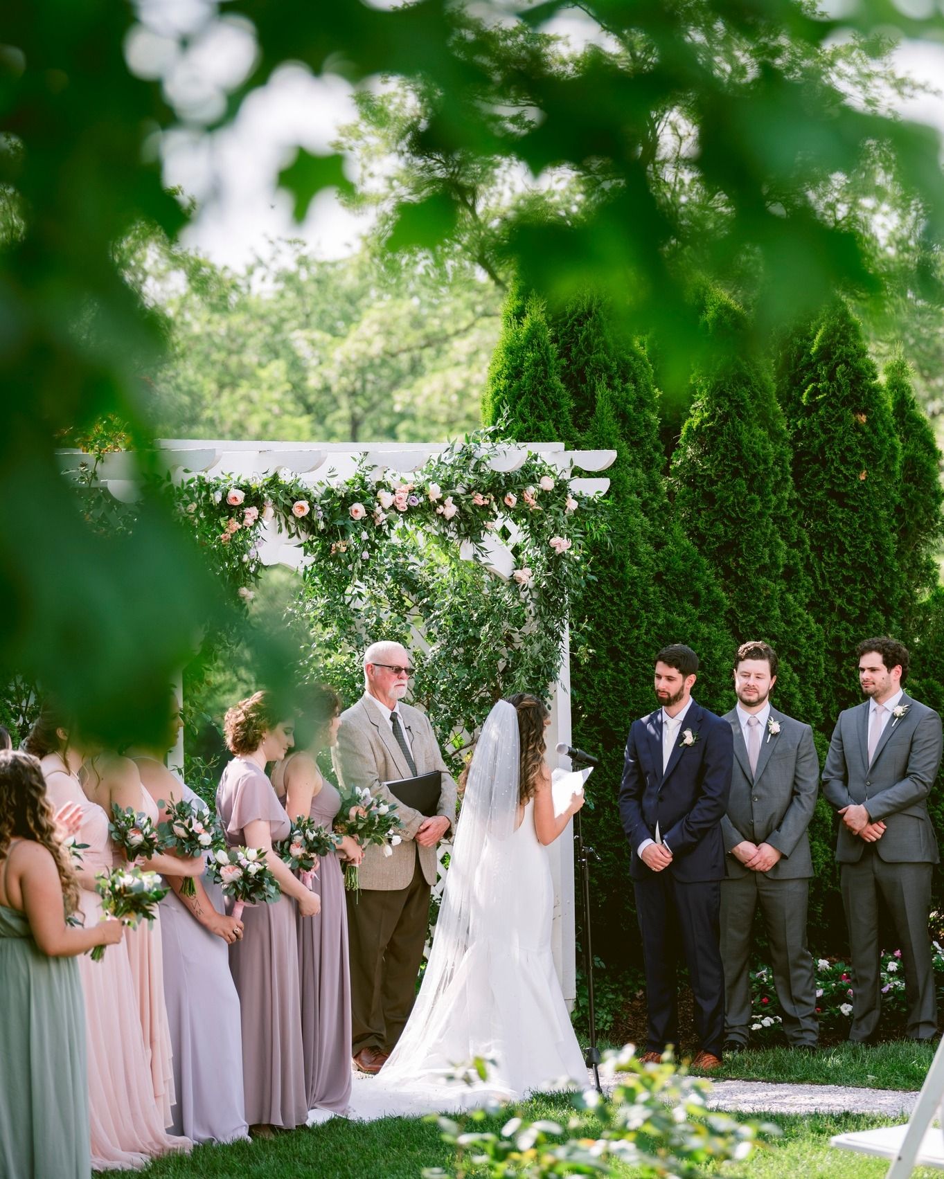 Wedding party stands in line during outdoor garden ceremony under green trees and natural lighting at Maryland wedding venue Antrim 1844.