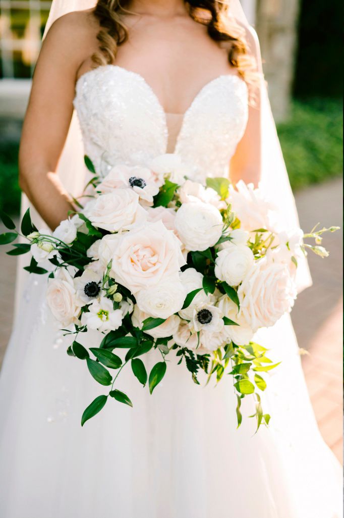 Beautiful bridal bouquet with white roses and anemones against a white strapless wedding dress bodice.