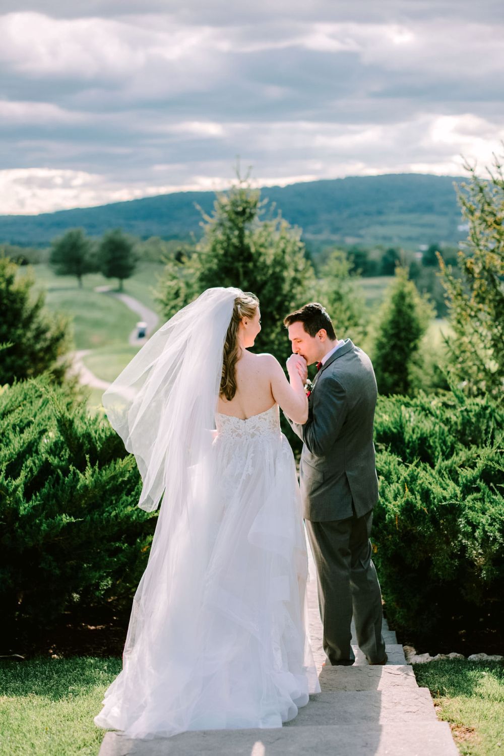 A couple shares an intimate moment on their wedding day against a backdrop of rolling hills and evergreen trees.