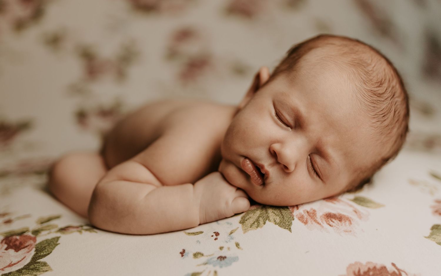Peaceful newborn baby sleeping on a floral blanket in a soft, dreamy portrait photography setting.