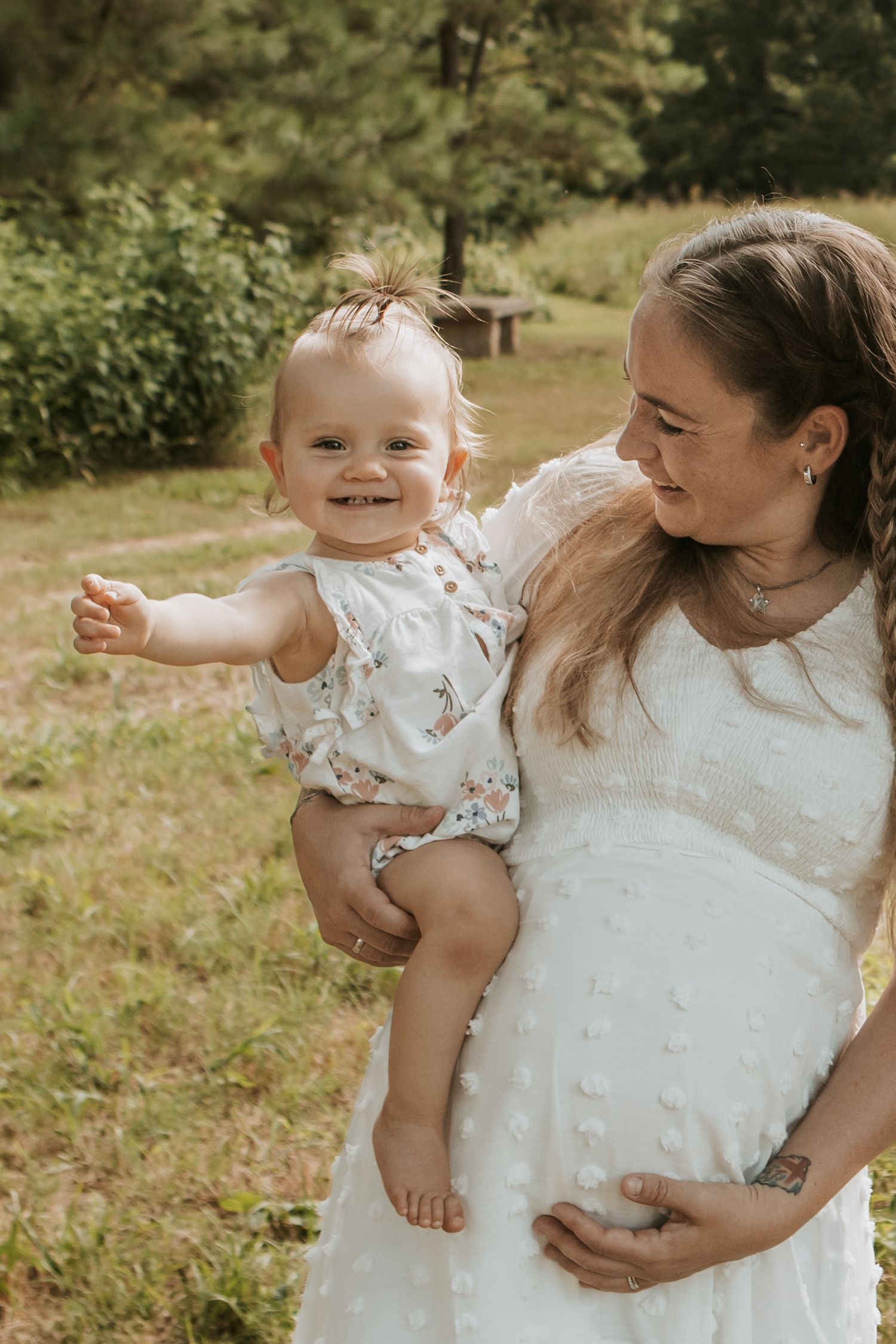 Pregnant mother smiles at toddler girl while posing with Keely King Photography in Jenks Oklahoma at Coal Creek Farm.