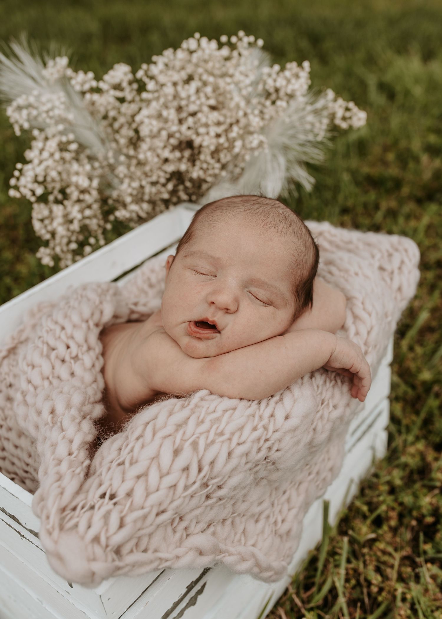 Sleeping newborn baby wrapped in pink knit blanket inside white wooden crate with white flowers in Big Cabin Oklahoma