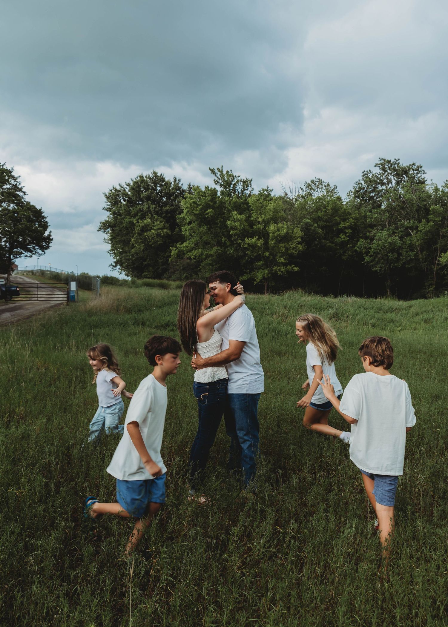 Family of six in matching white shirts sharing a kiss in a green meadow during outdoor family photo session.