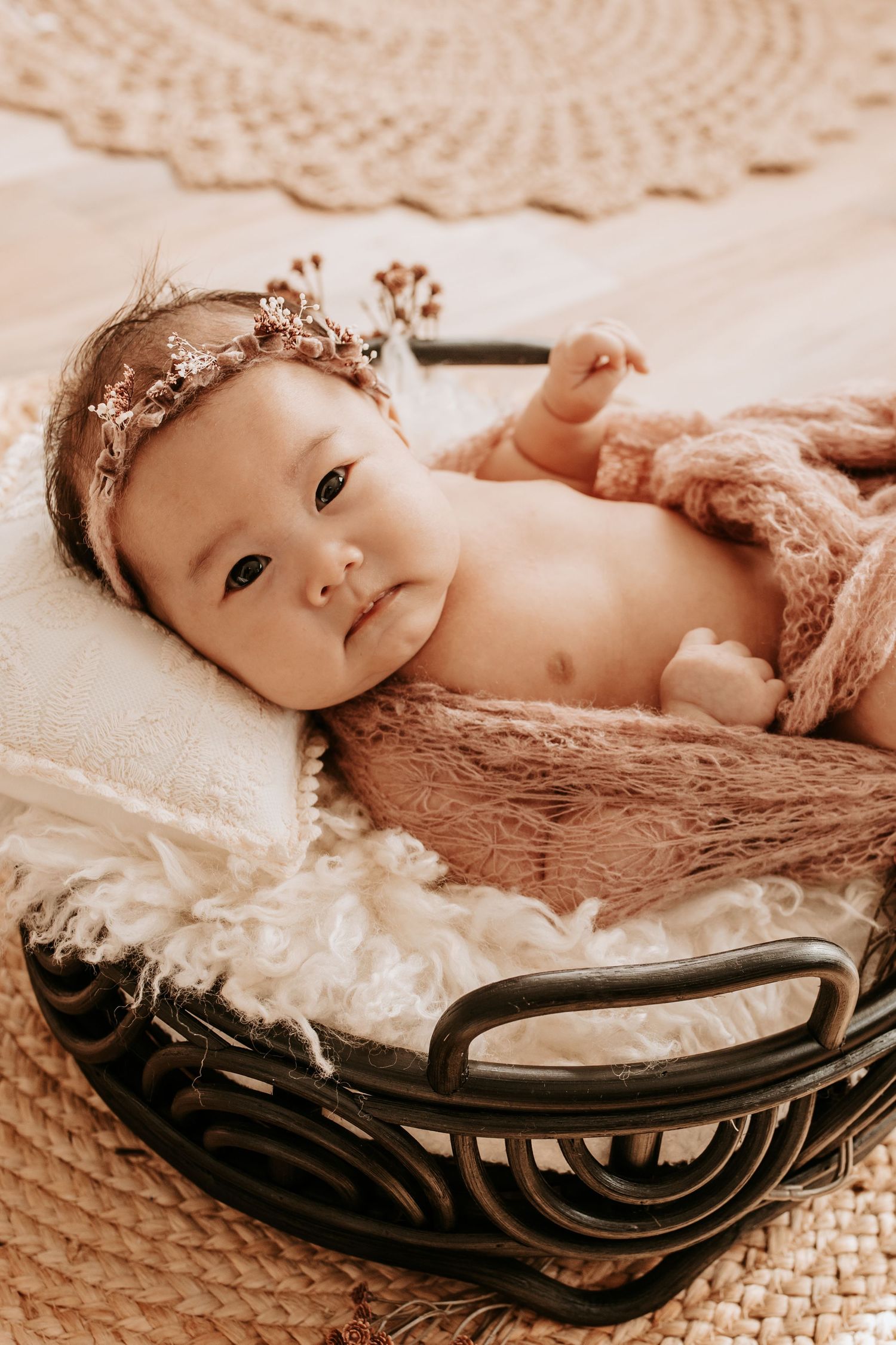 Newborn baby girl wearing a floral headband lying in a wicker basket with soft white and pink blankets taken by Keely King in Tulsa Oklahoma