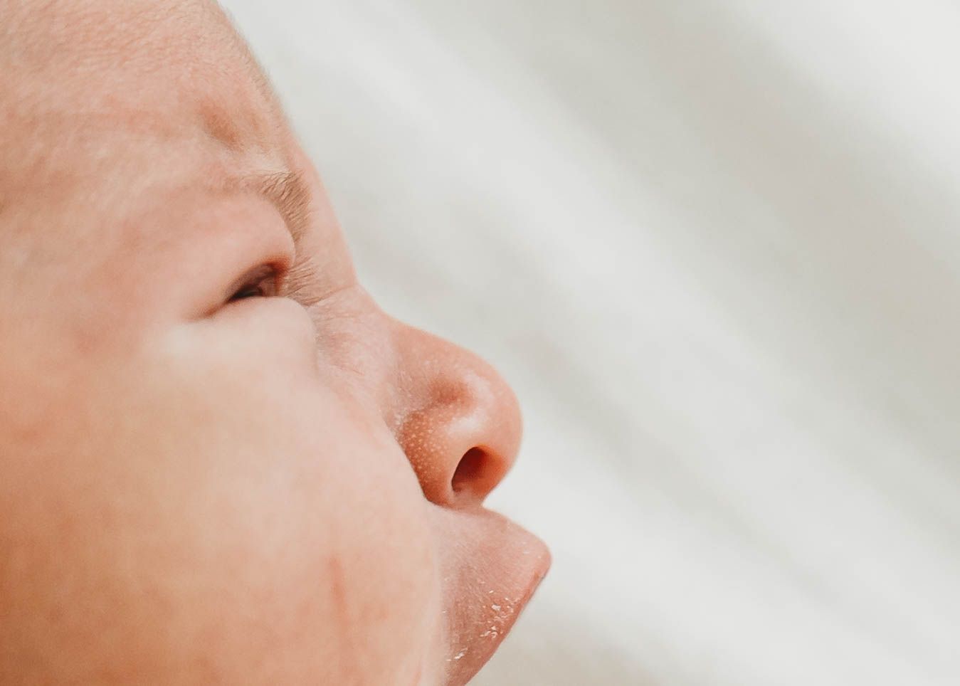 Close-up profile of a sleeping newborn baby with soft skin and delicate features against a white background.
