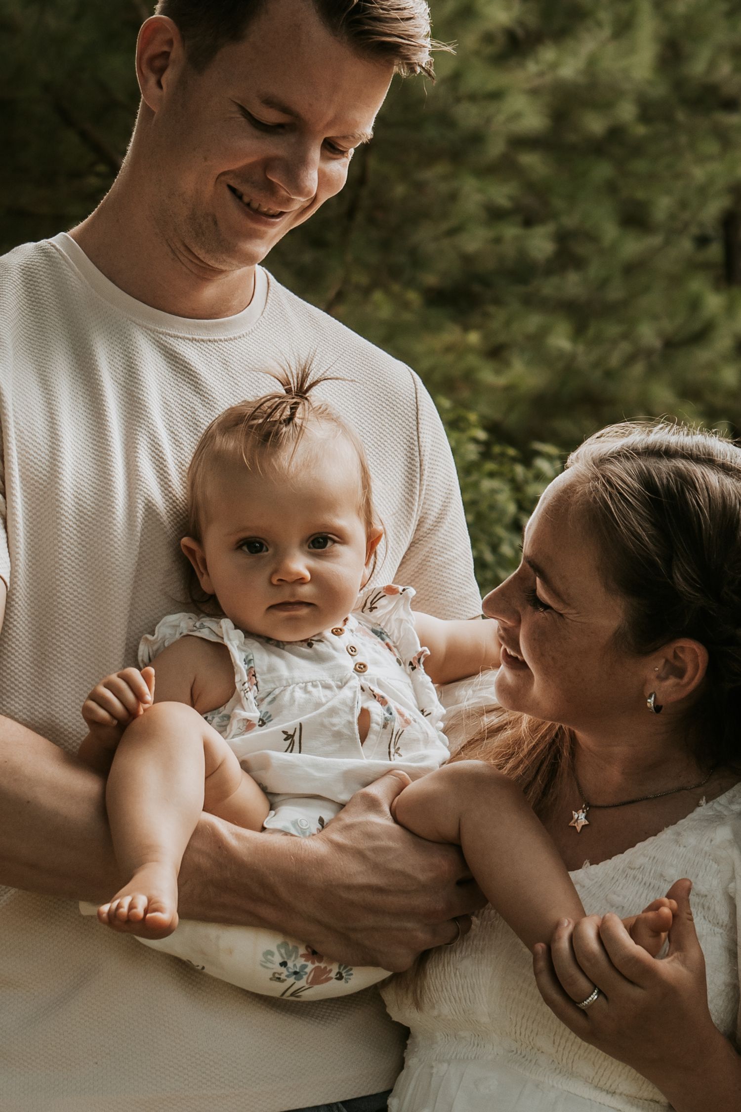 Happy young family with parents smiling at their baby girl in a floral outfit at Coal Creek Farm with Keely King Photography in Jenks.