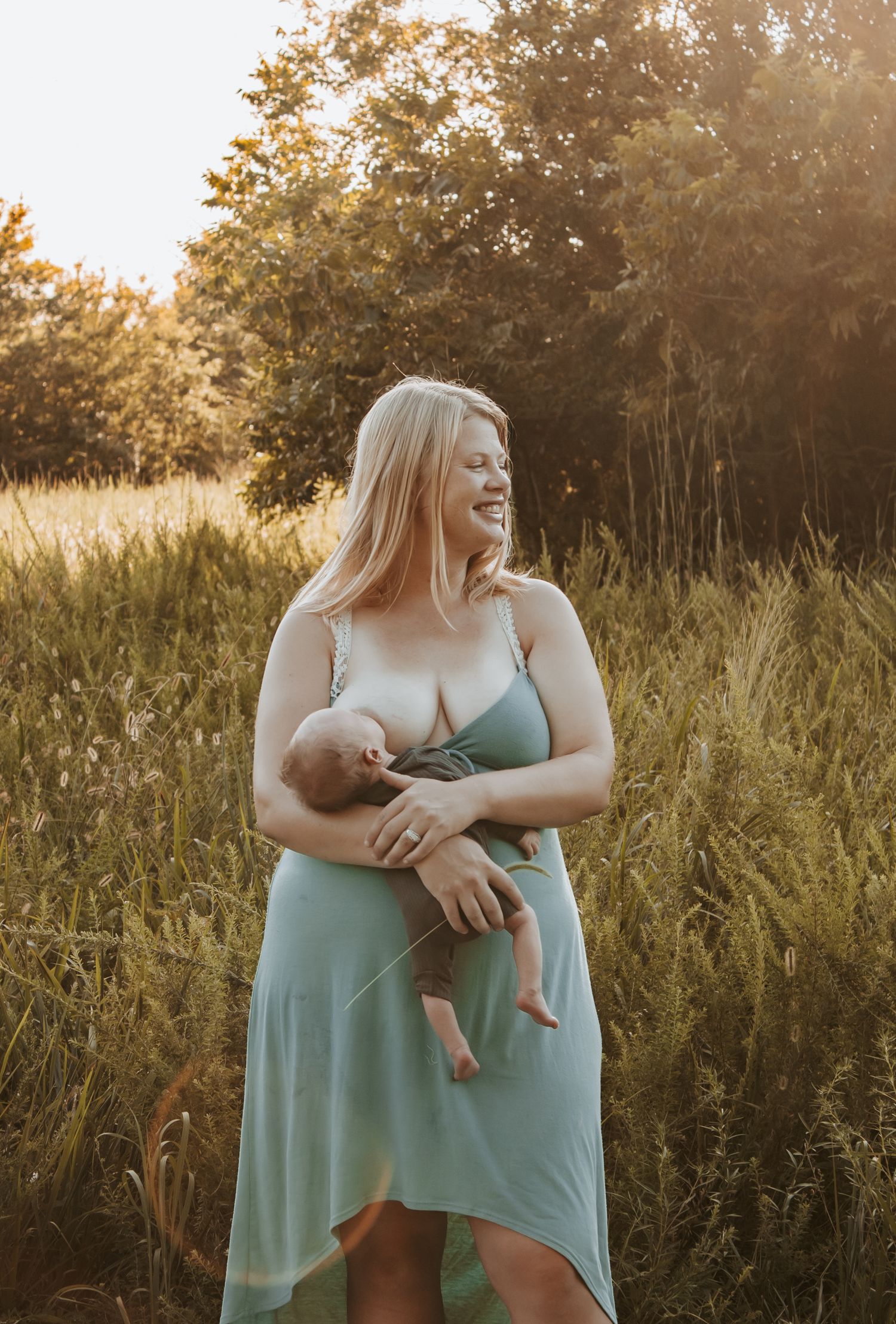Keely King Photography captures radiant mother with confidence while breastfeeding newborn during golden hour in Claremore at an open field