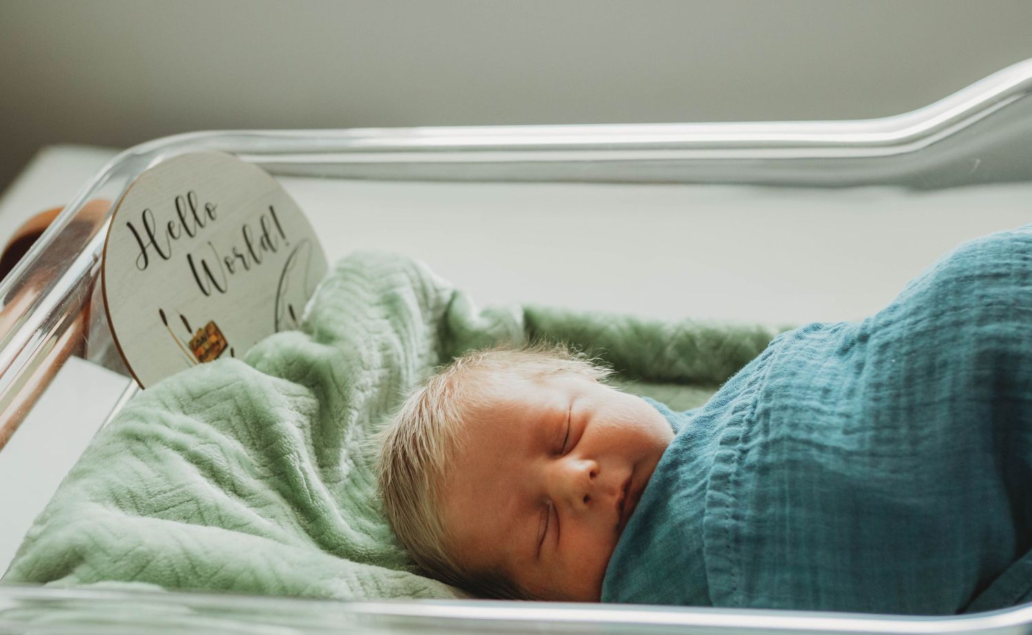fresh forty-eight style hospital session of a newborn boy with long blonde hair wrapped in a blue blanket in the bassinet.