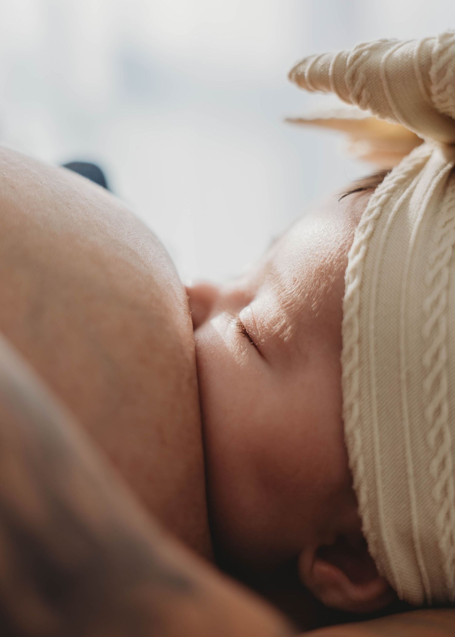 Newborn baby breastfeeding peacefully while wearing a cream bow headband.