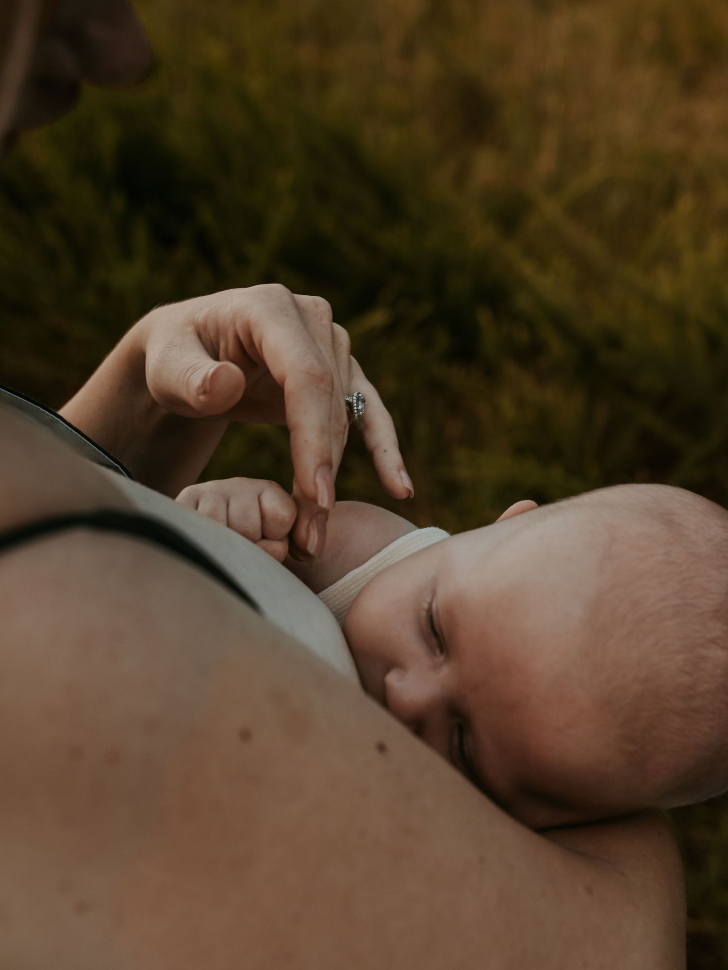 Detail shot of mother caressing newborn's hand while breastfeeding during Keely King Photography's Breastfeeding Mini session in Claremore