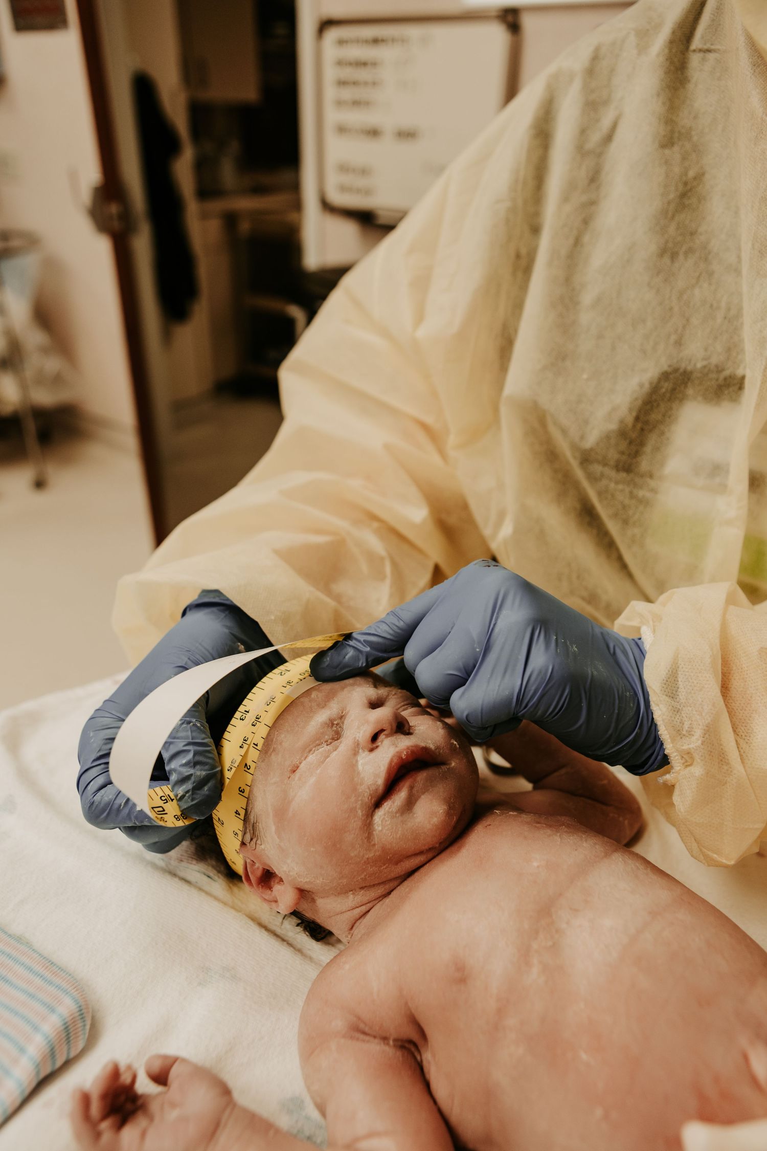 Medical professional in gloves placing a hat on a newborn baby lying on a white blanket in a hospital.