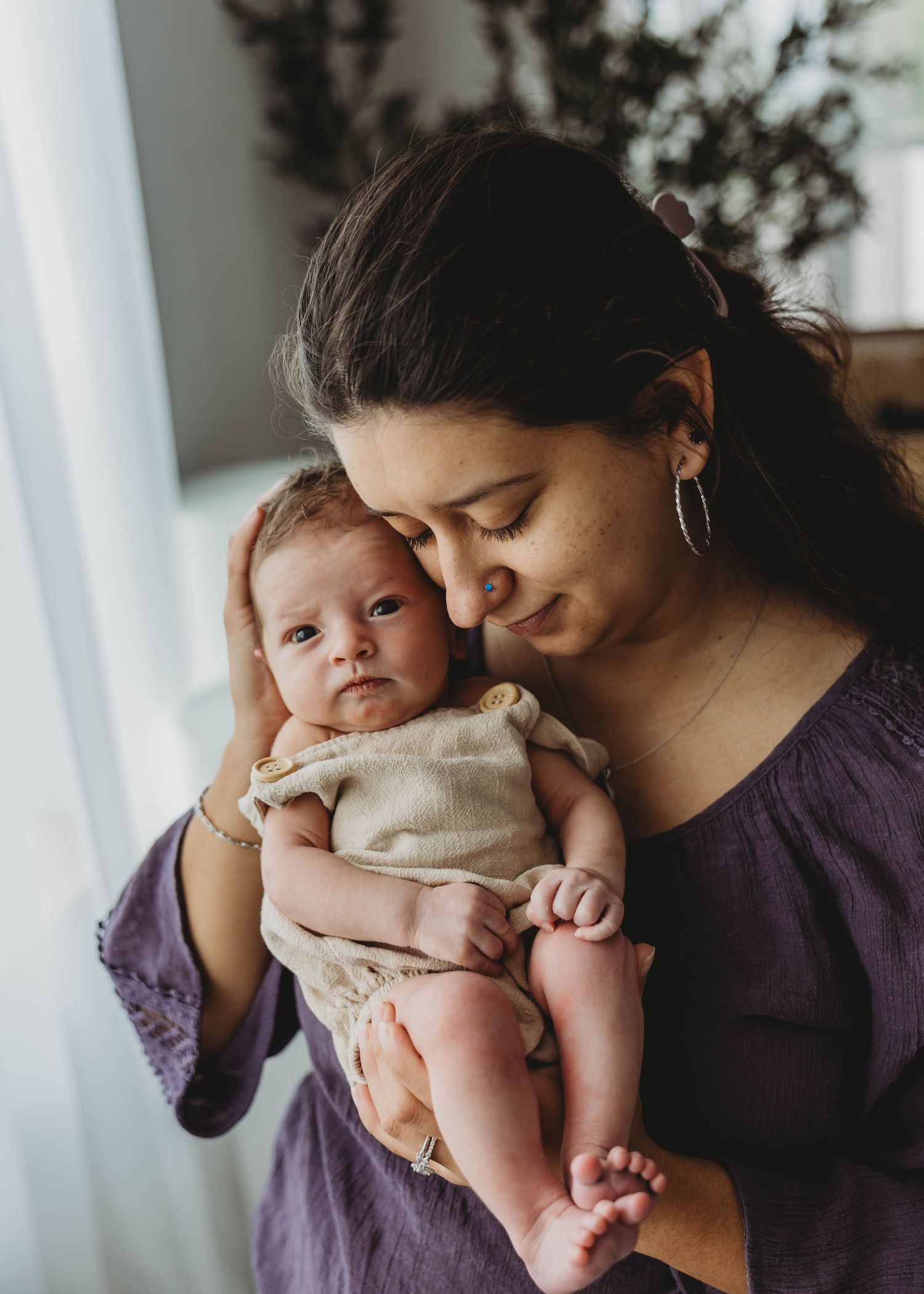 A mother tenderly holds her newborn baby close, touching foreheads in an intimate moment of love.