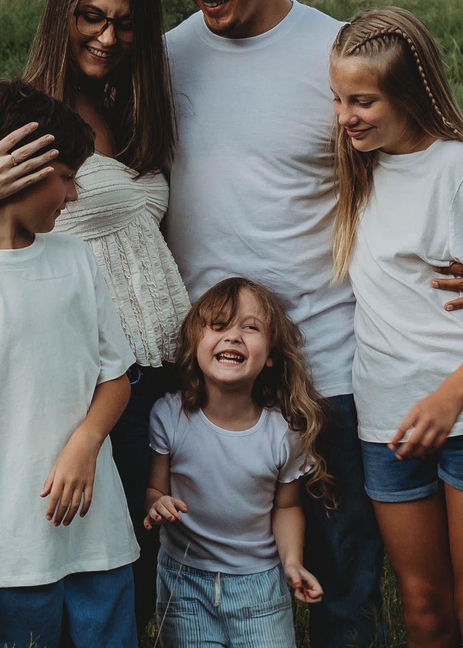 Joyful family of five in white shirts laughing together during a candid outdoor family portrait session.