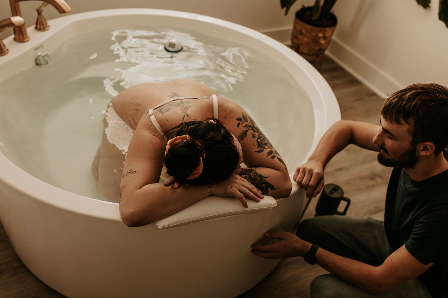 Woman laboring in a round white soaking tub during a water birth with a supportive partner beside her.