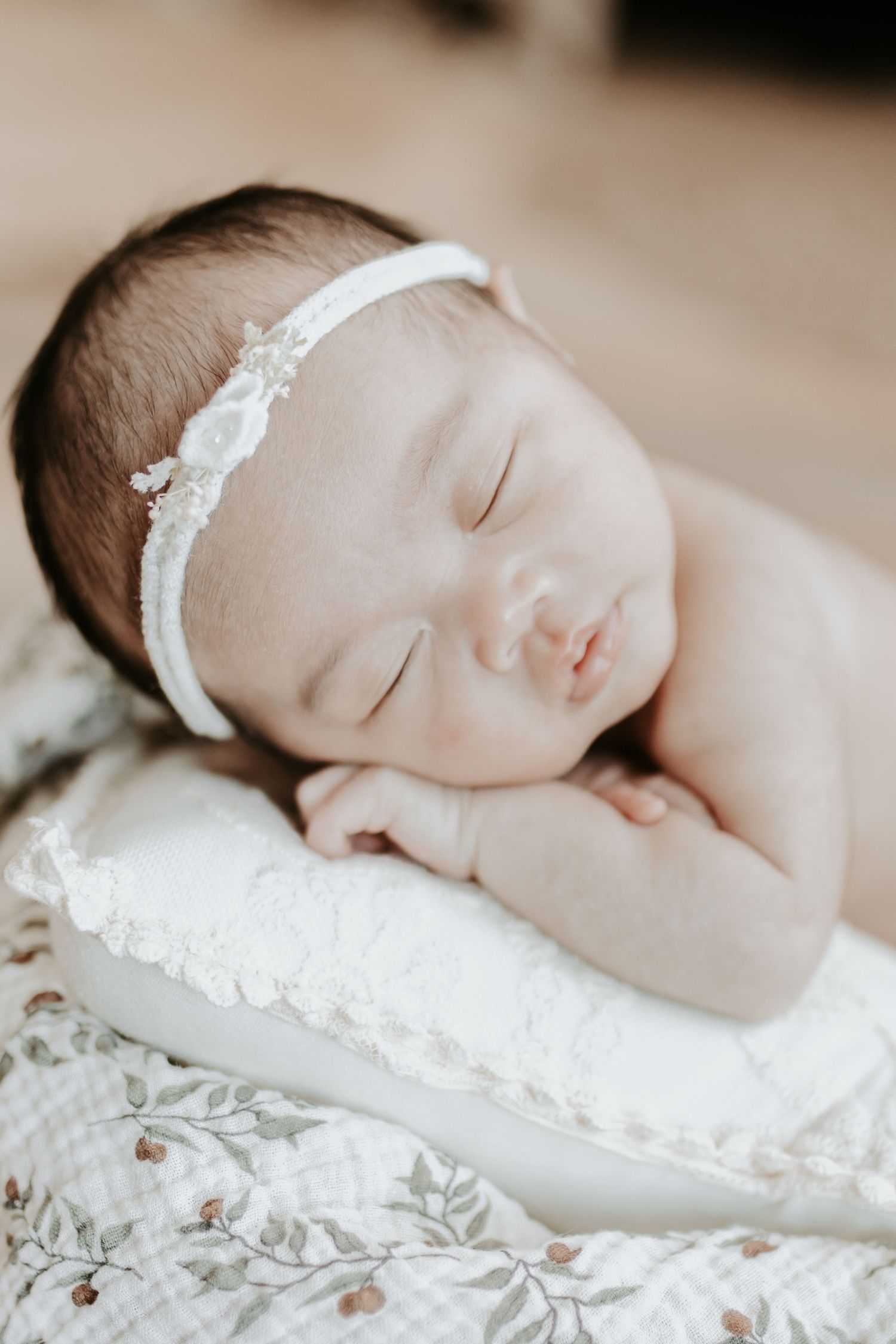 Sleeping newborn baby girl wearing a delicate white lace headband, resting peacefully on a small white pillow.