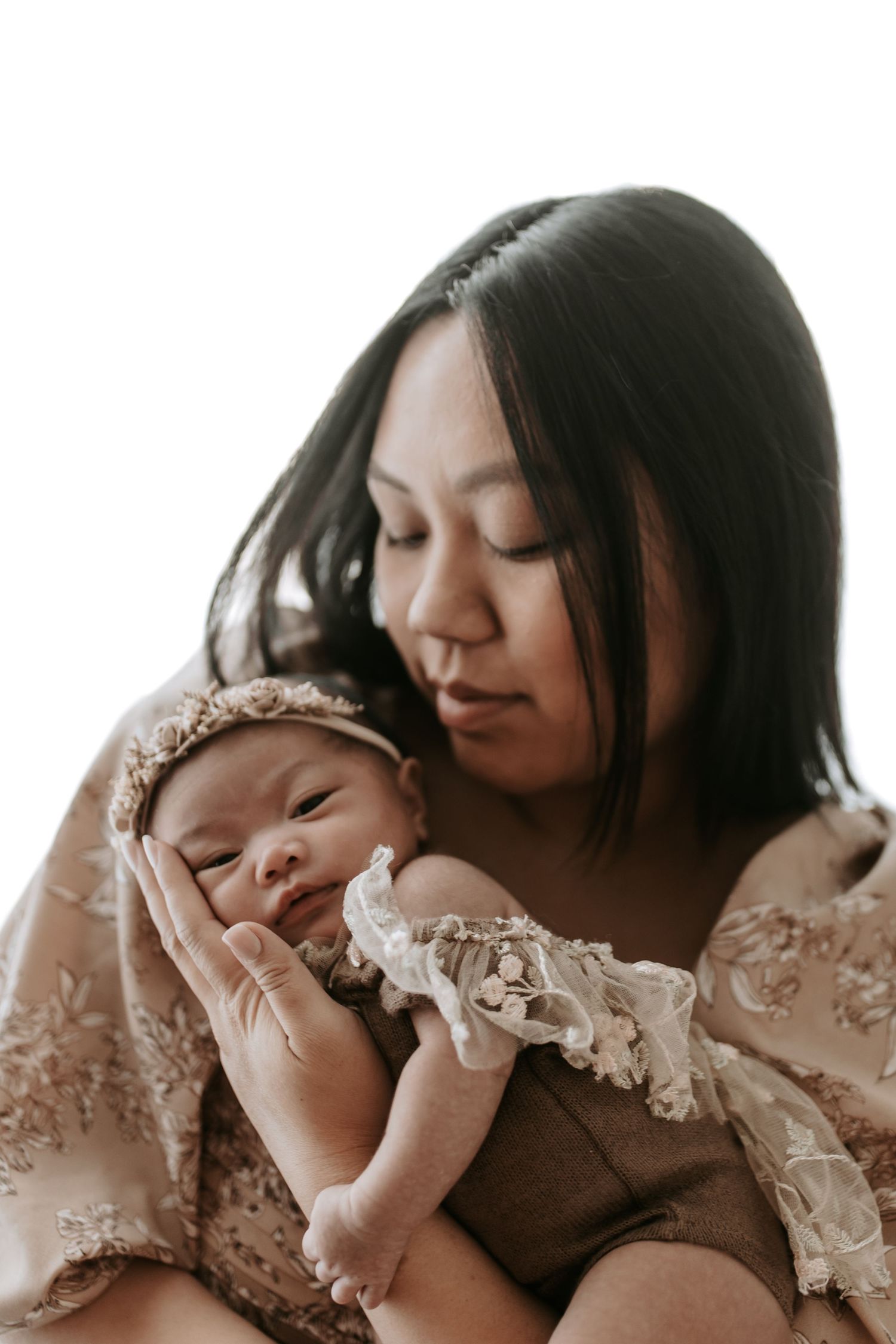 A mother tenderly holds her newborn baby dressed in a lace bonnet and floral wrap in a studio portrait.