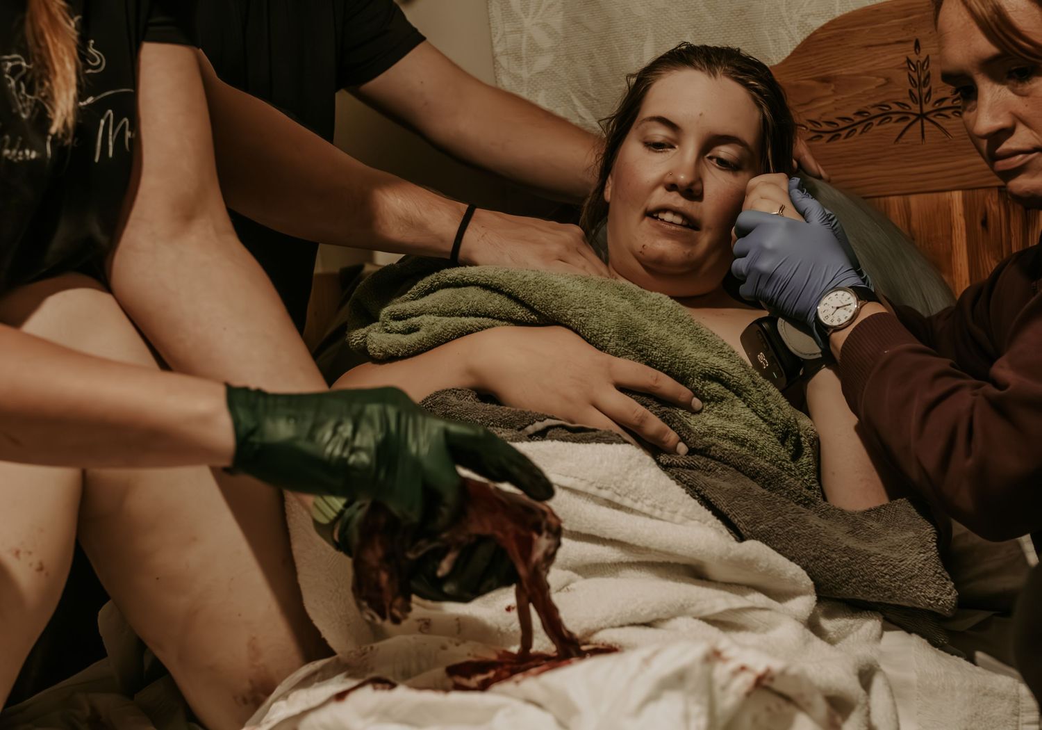 Woman holding her newborn baby directly after birth looking at her placenta while laying in bed surrounded by her birth team in Mounds