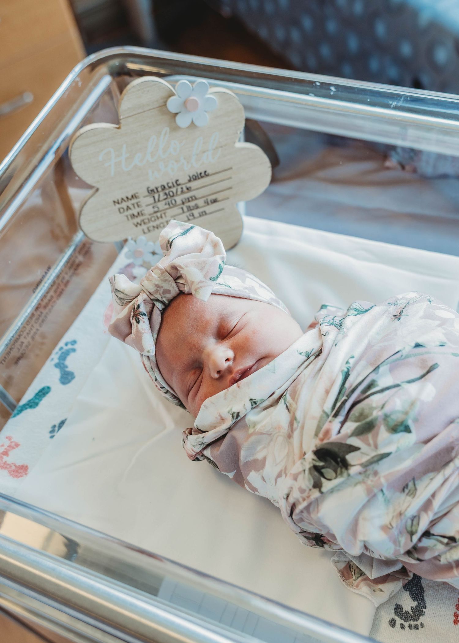 Sleeping newborn baby in hospital bassinet with Hello Baby name announcement sign.