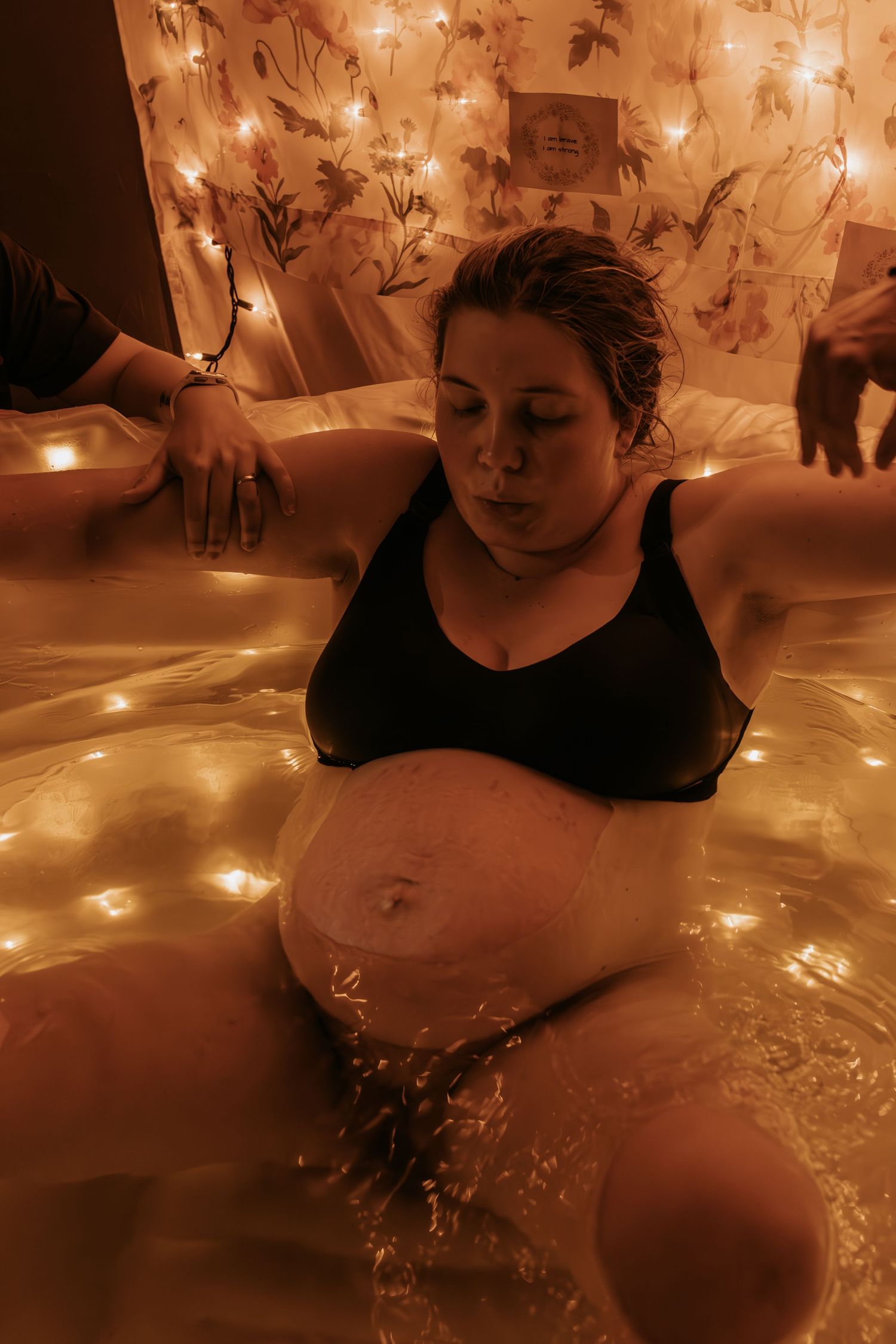 Woman labouring at home in a birthing tub breathing deep through a contraction in a warm room lit with fairy lights in Mounds Oklahoma