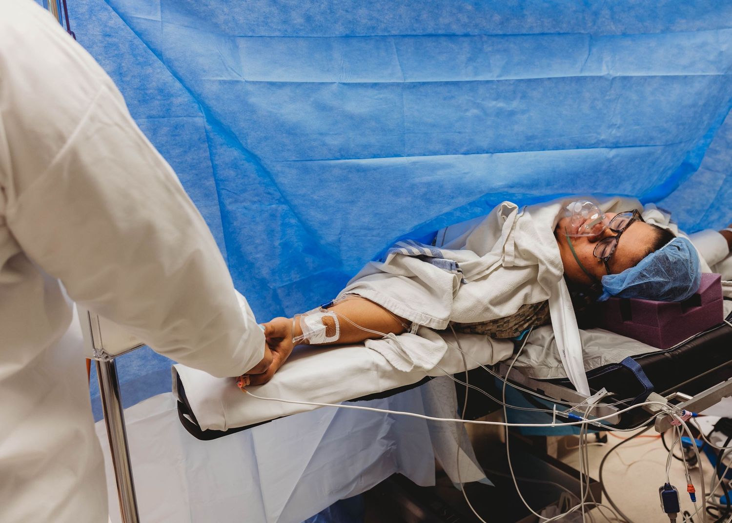 Medical professional holding patient's hand during surgical procedure in operating room with monitoring equipment.