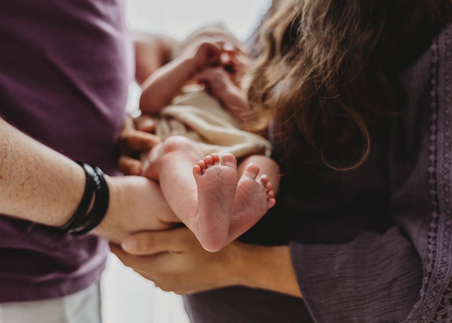 Close-up of newborn baby feet cradled in parents hands during fresh 48 newborn photography session.
