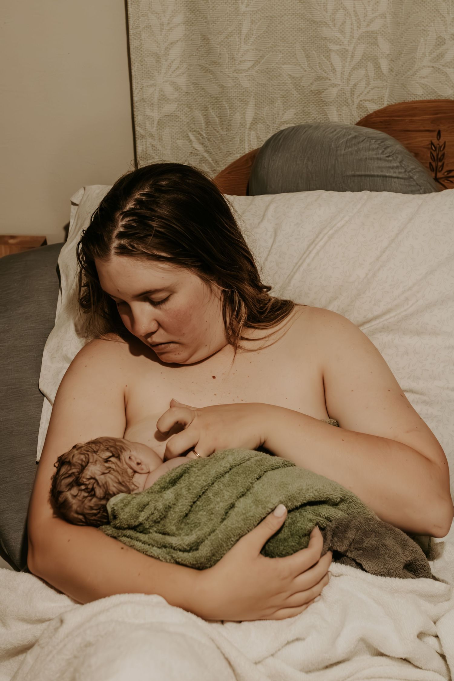 A mother breastfeeding her newborn baby wrapped in a green towel while resting in bed after a home birth in Mounds Oklahoma with Keely King