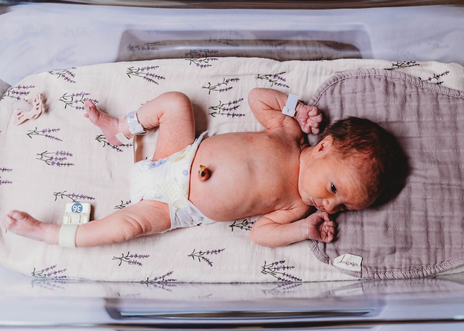 Newborn baby lying in hospital bassinet on patterned blanket, wearing diaper and ID bracelet after birth.