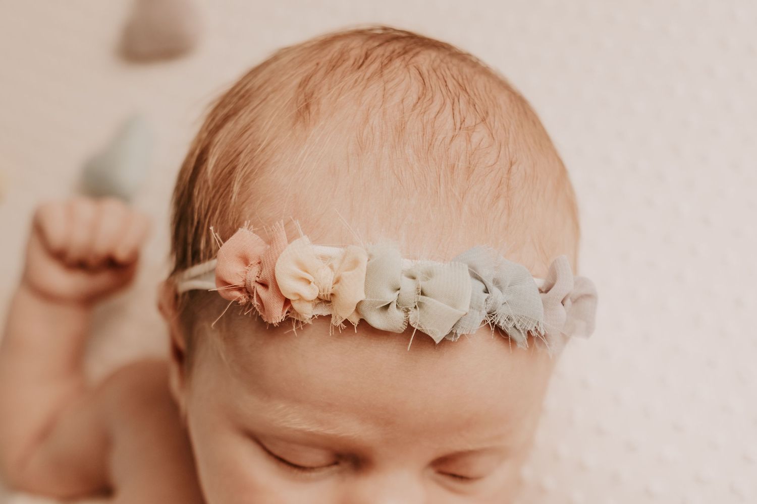 Close-up of a newborn baby wearing a delicate floral headband with pastel rainbow bows posed by Keely King Photography in Chelsea Oklahoma