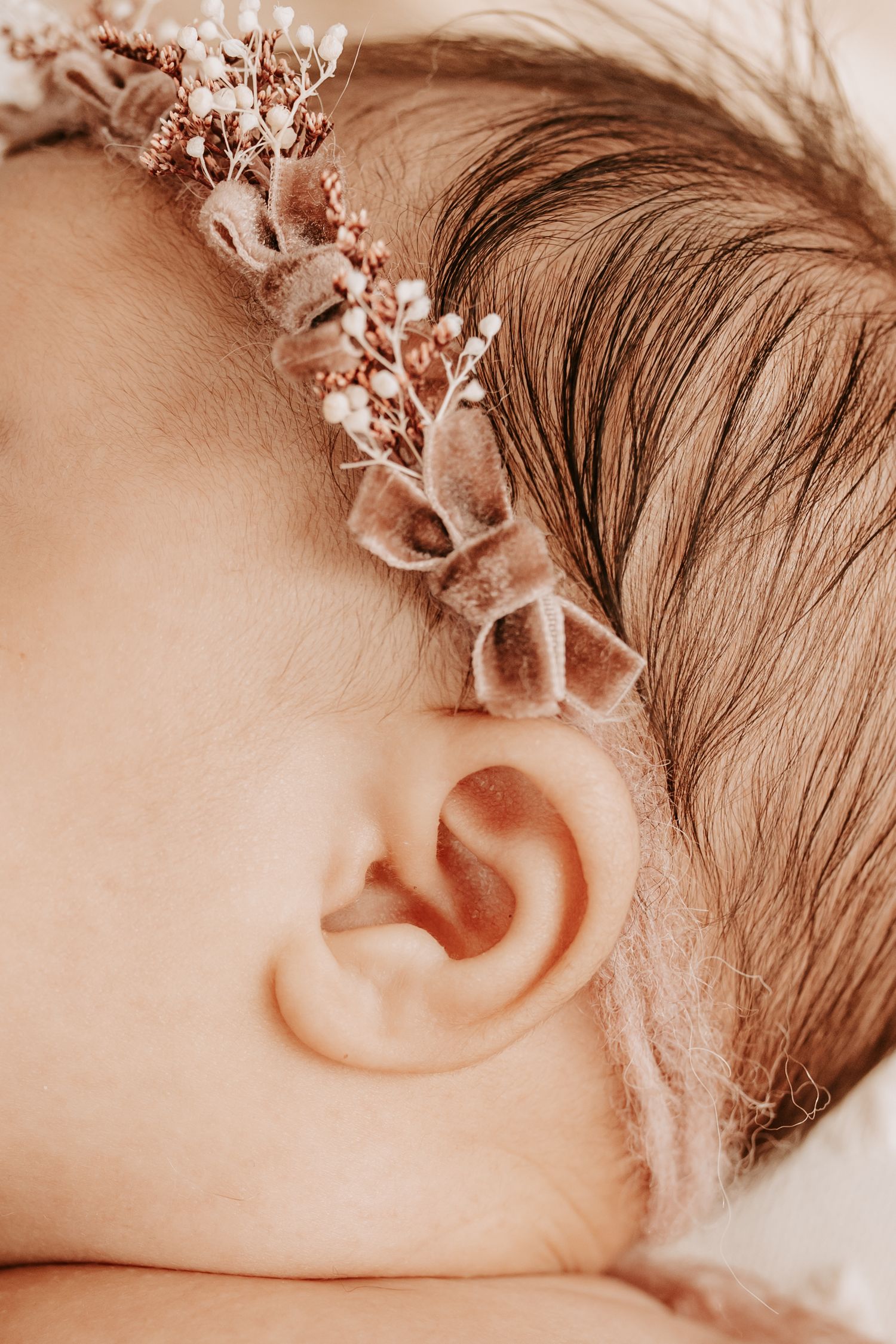 Close-up of a sleeping baby wearing a delicate floral headband with tiny pink blooms and velvet leaves.