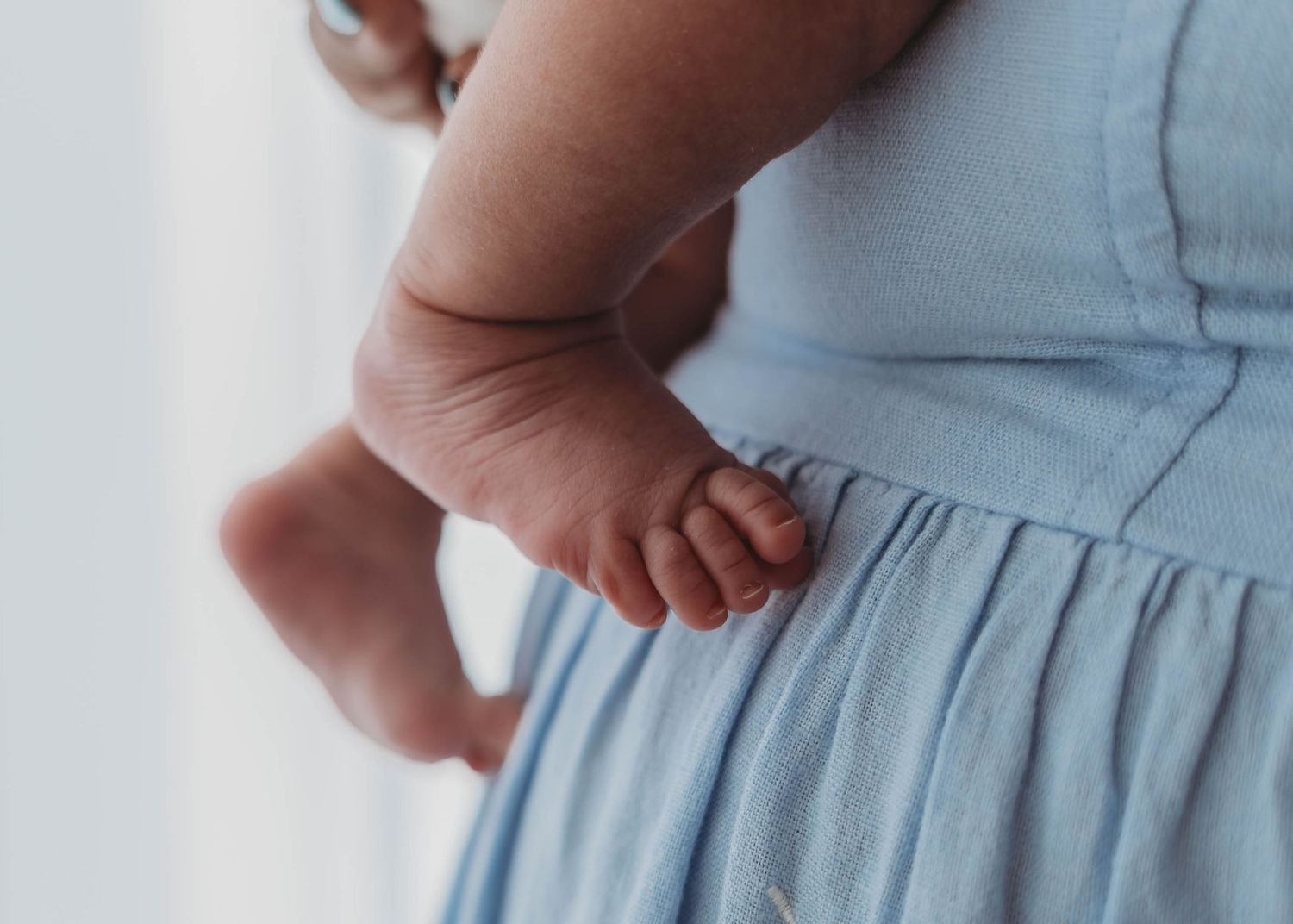 Close-up of tiny baby feet resting against a woman in a soft blue dress.