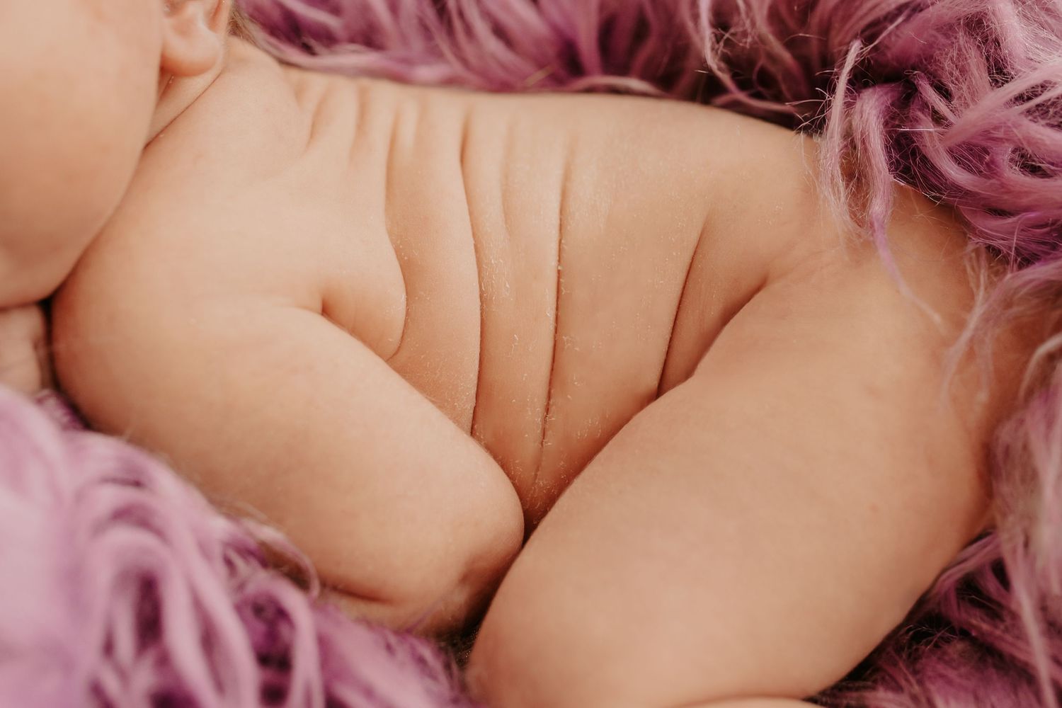 Close-up of chubby newborn baby back and legs resting on soft pink fluffy fur blanket.