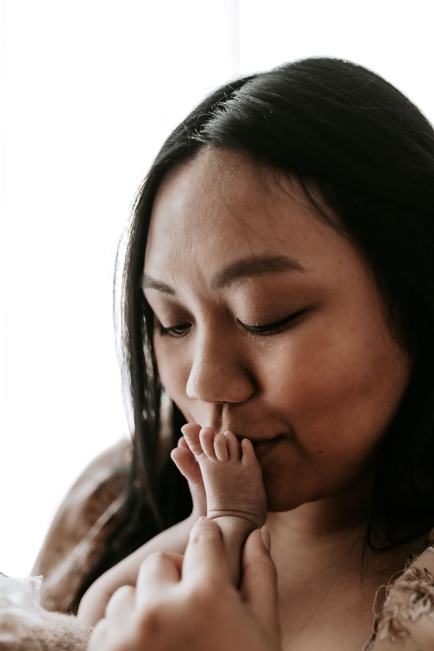 A tender mother gently kisses her newborn baby's tiny feet in a soft, intimate portrait.