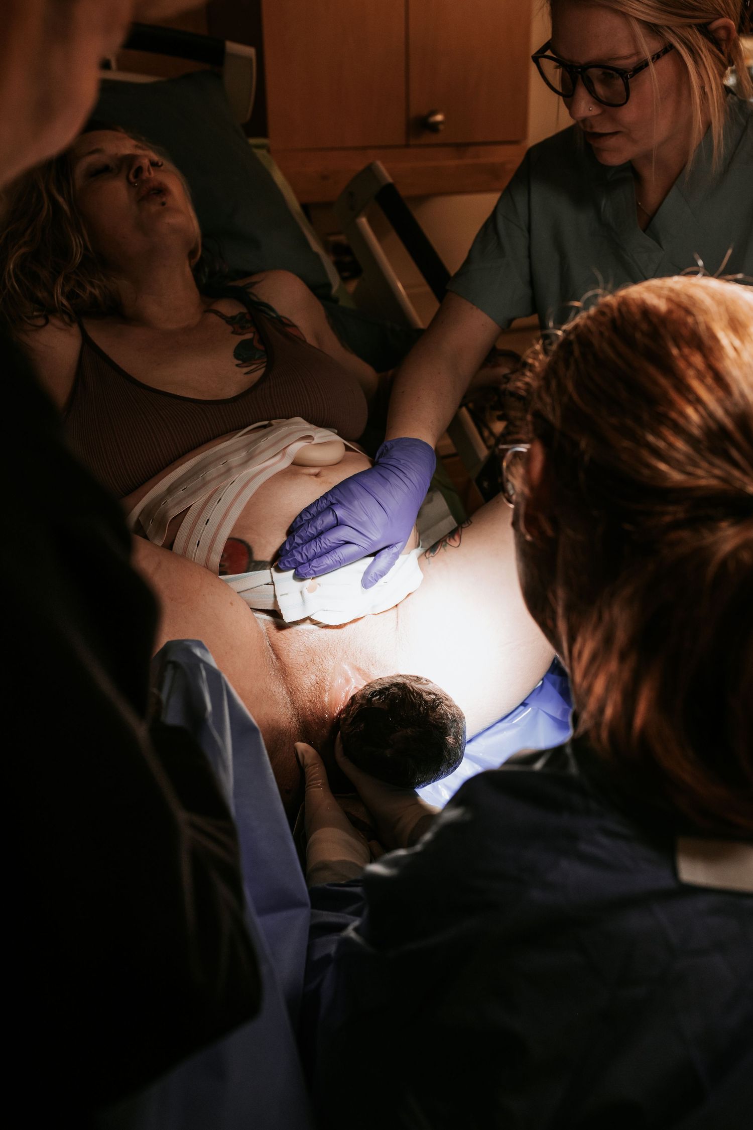 Medical team assisting a woman during childbirth in a hospital delivery room under bright surgical lighting.
