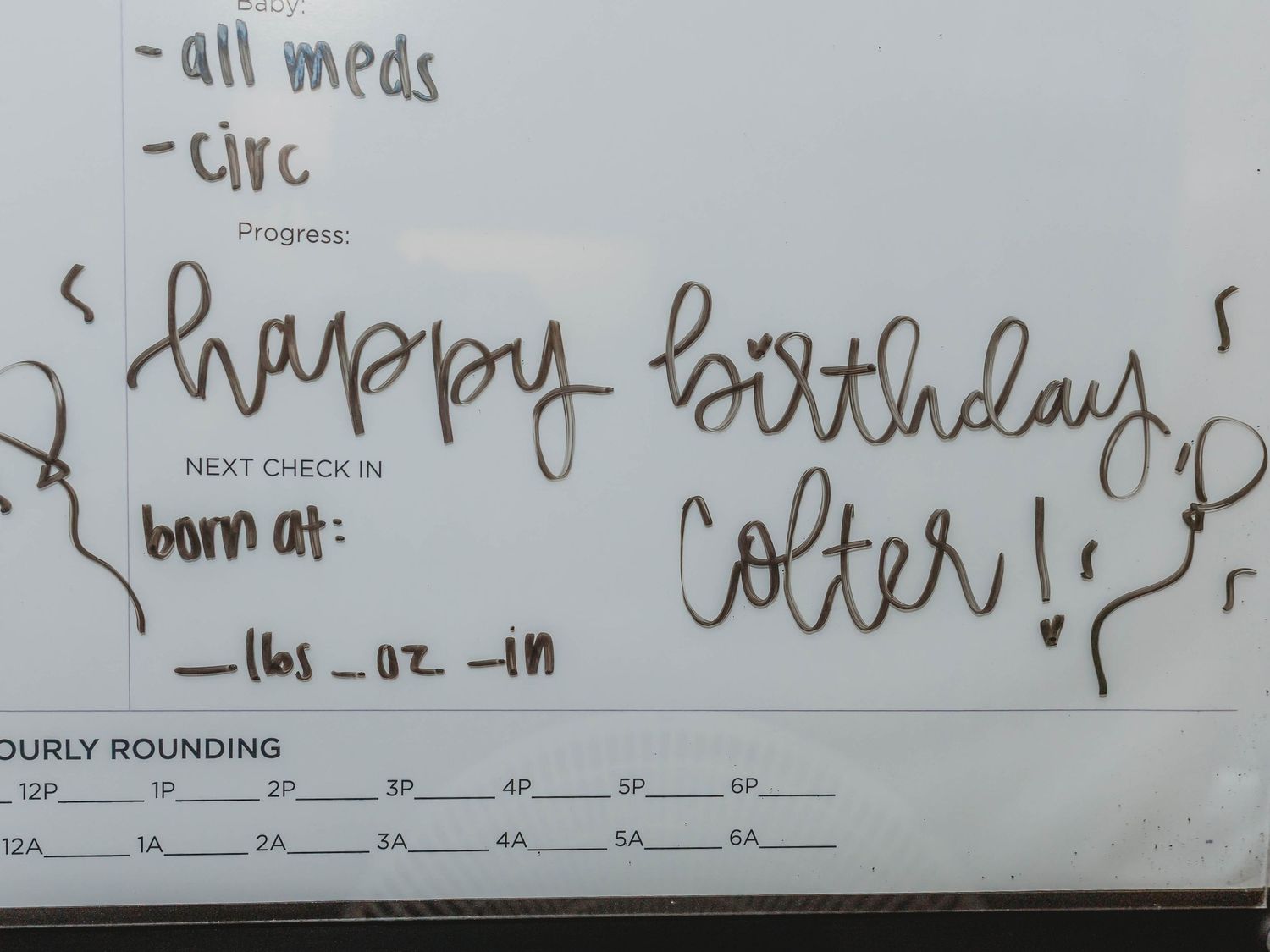 Hospital whiteboard with handwritten Happy Birthday Colter message, blank birth stats fields, and an hourly rounding chart.