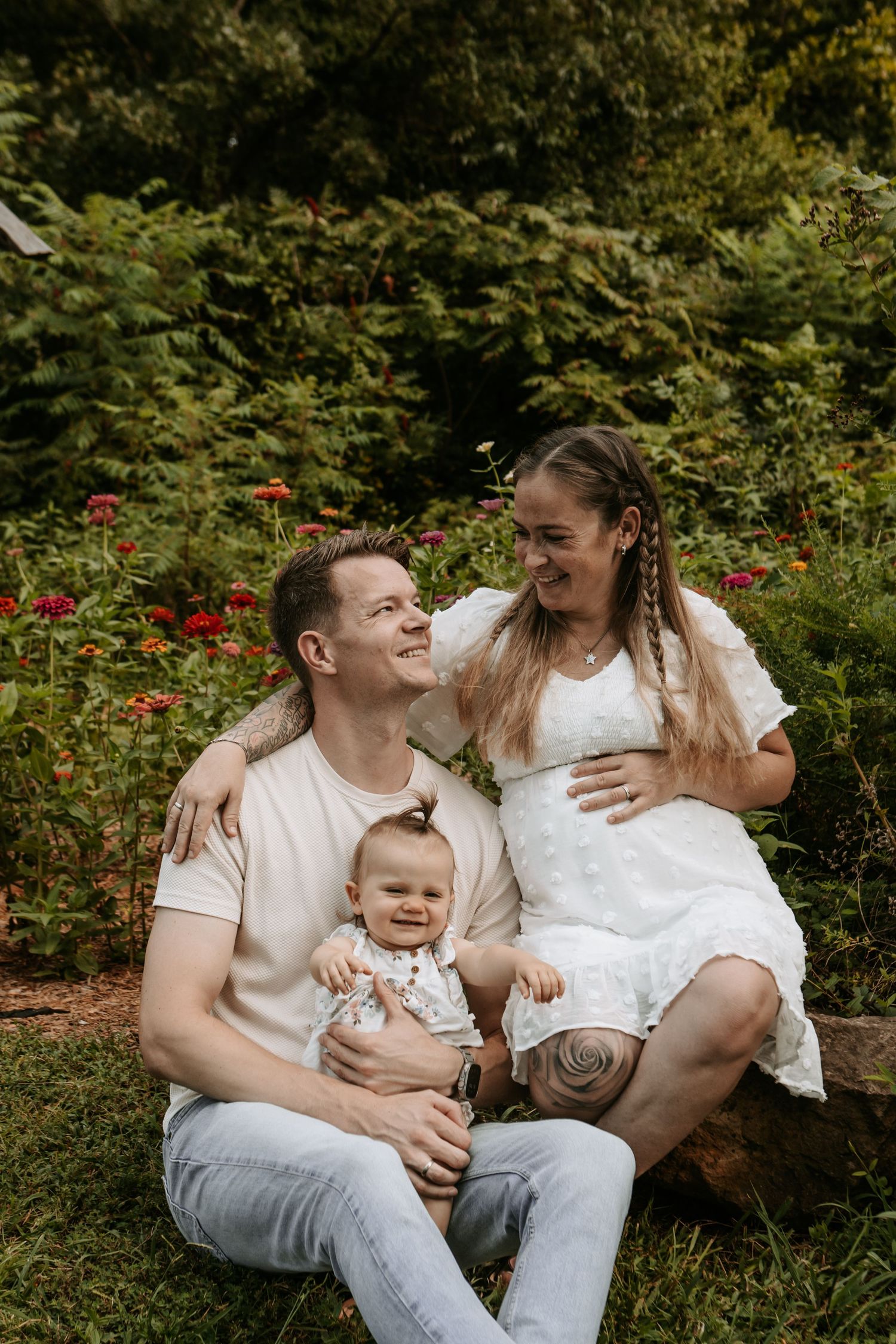 vertical shot of family of three sitting infront of a flower patch at Coal Creek Farm in Jenks by Keely King Photography.