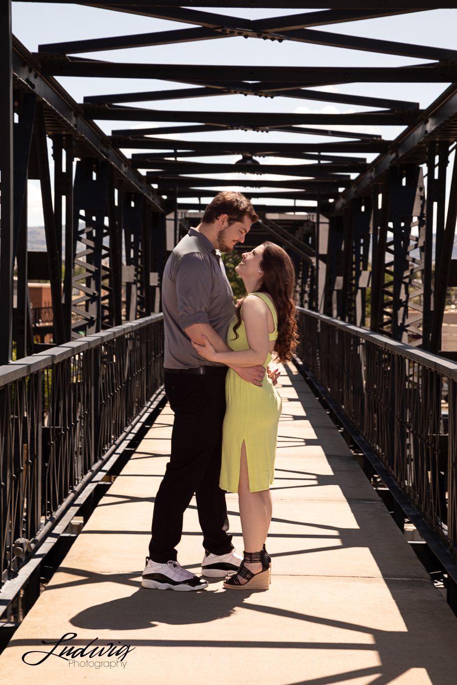 Engaged couple on Downtown Footbridge, Laramie, Wyoming. The couple gazes at each other with love at golden hour. Downtown Laramie in back.