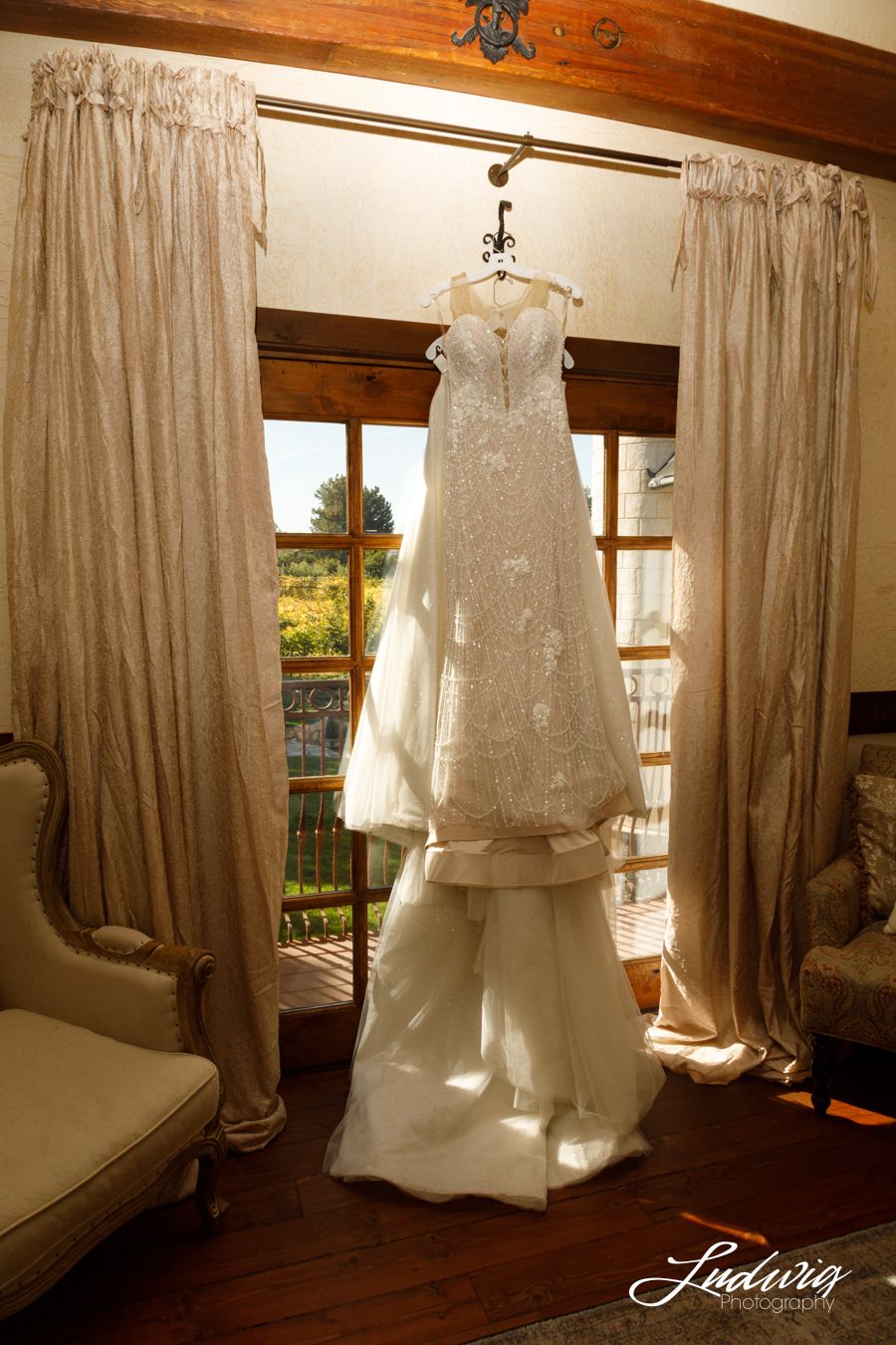 Wona Bridal Gown hanging in the window adorned with pearls and lace naturally lit at Wadley Farms, Lindon, Utah before a princess wedding.