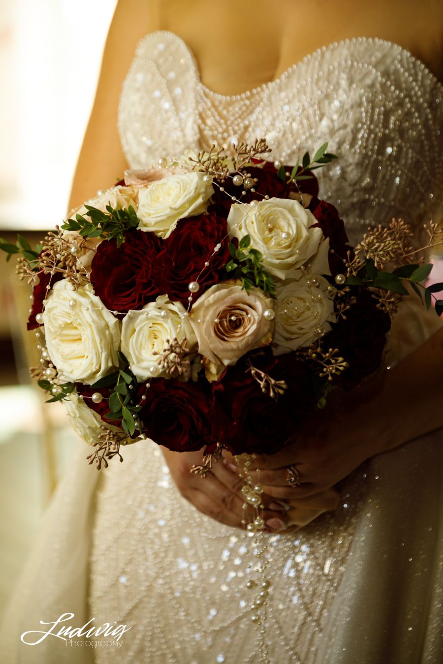 White and burgundy rose bouquet with pearls and rose gold accents at Wadley Farms. Bride's Wona bridal dress sparkles in the background.