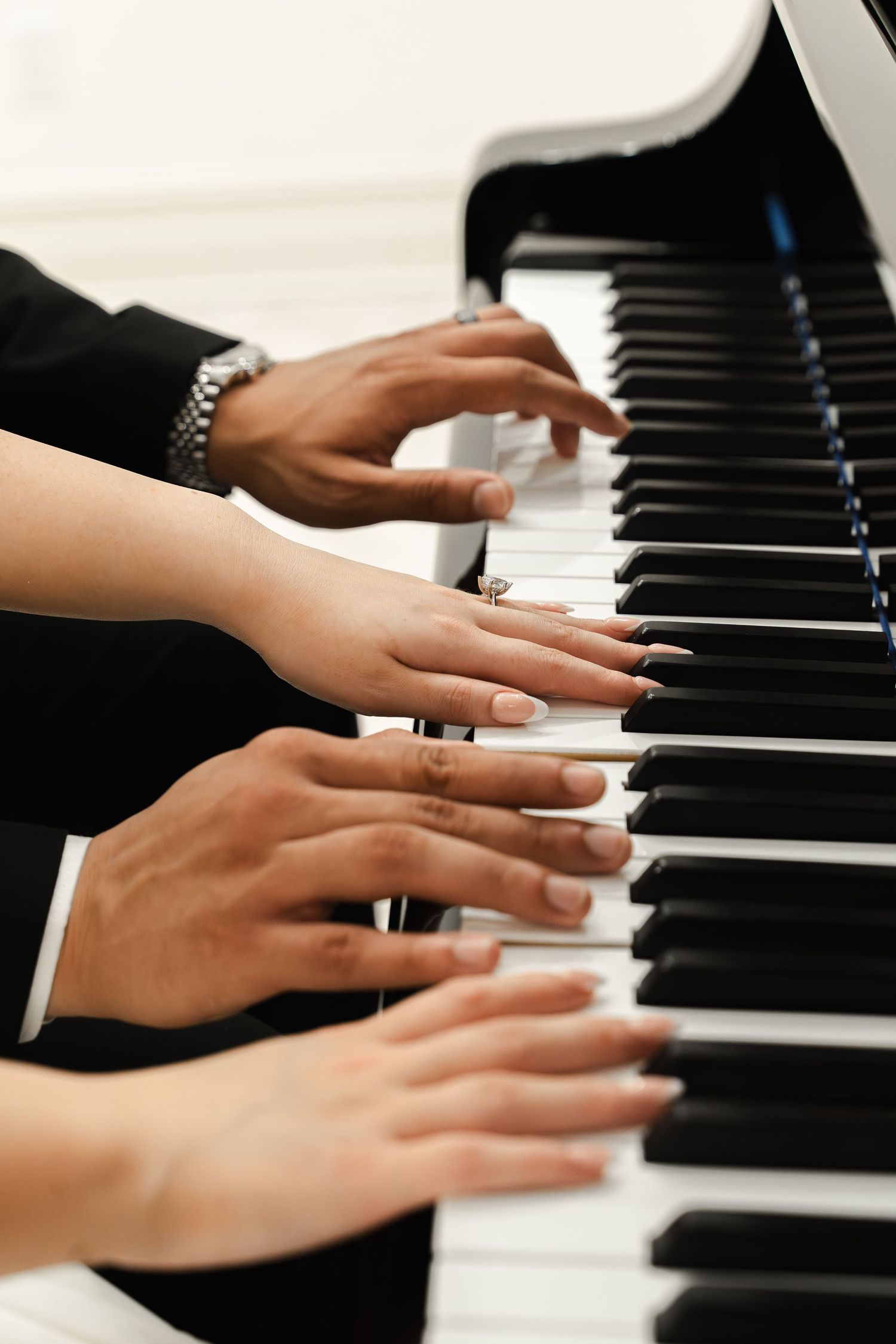 Two people playing piano together, hands visible with a diamond ring and silver bracelet.
