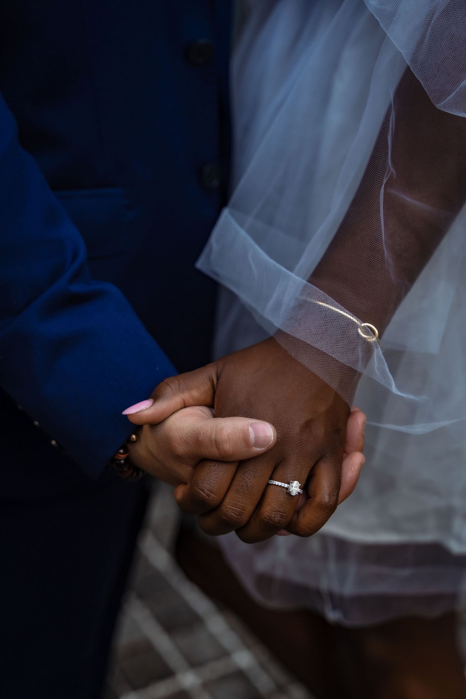 Close-up of interracial couple holding hands, bride wearing diamond engagement ring and delicate gold bracelet.