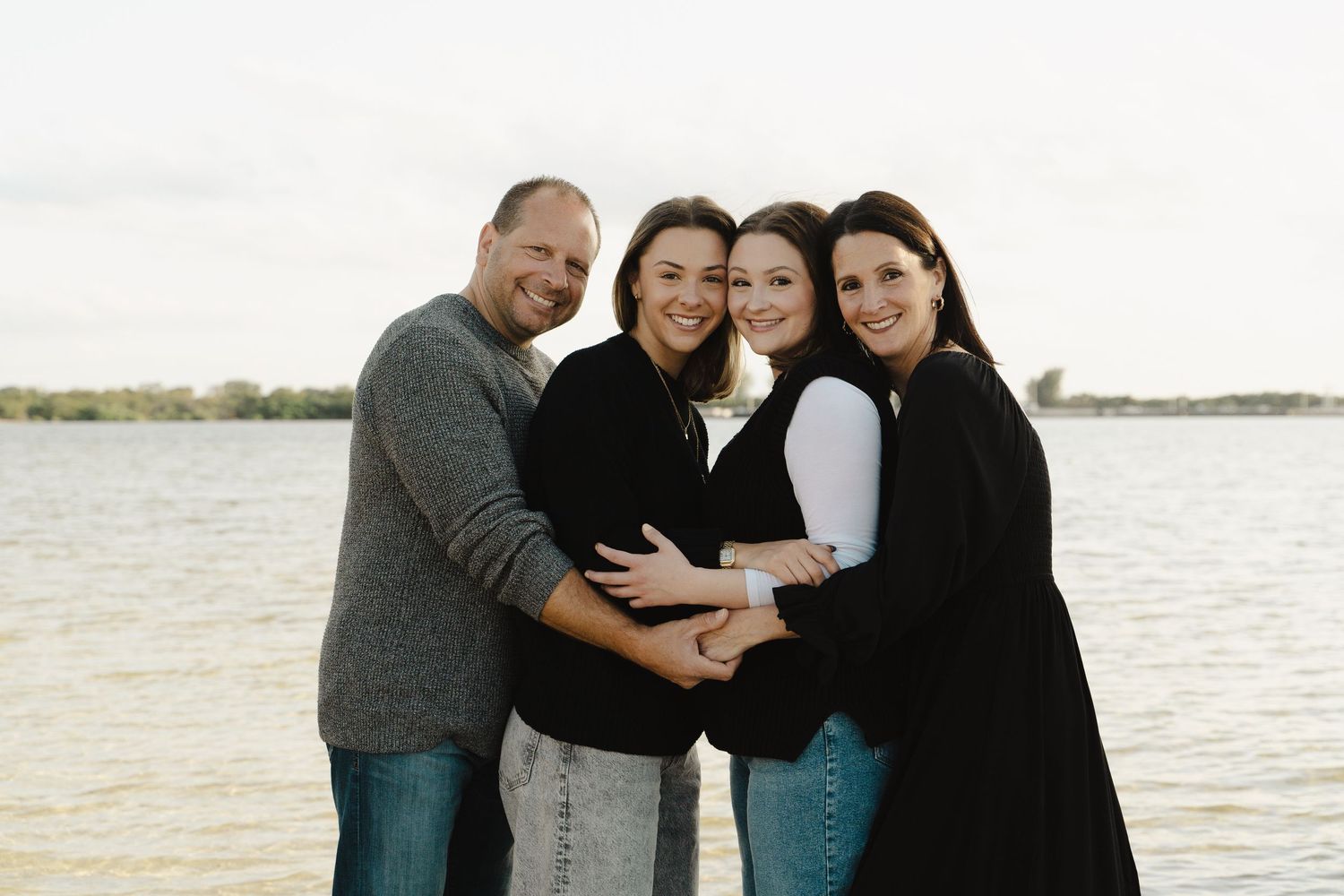 Happy family of four posing together near a lake with smiles and warm embraces.