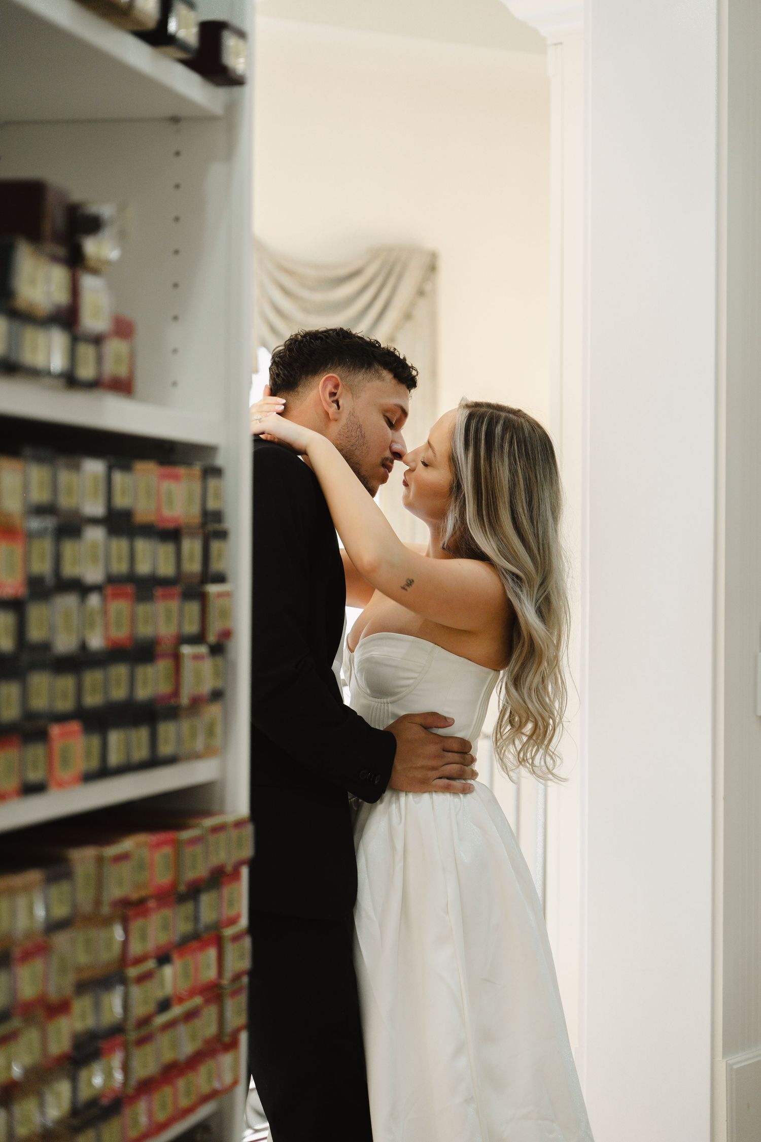 Bride and groom sharing an intimate moment embracing near a doorway with shelves in background.