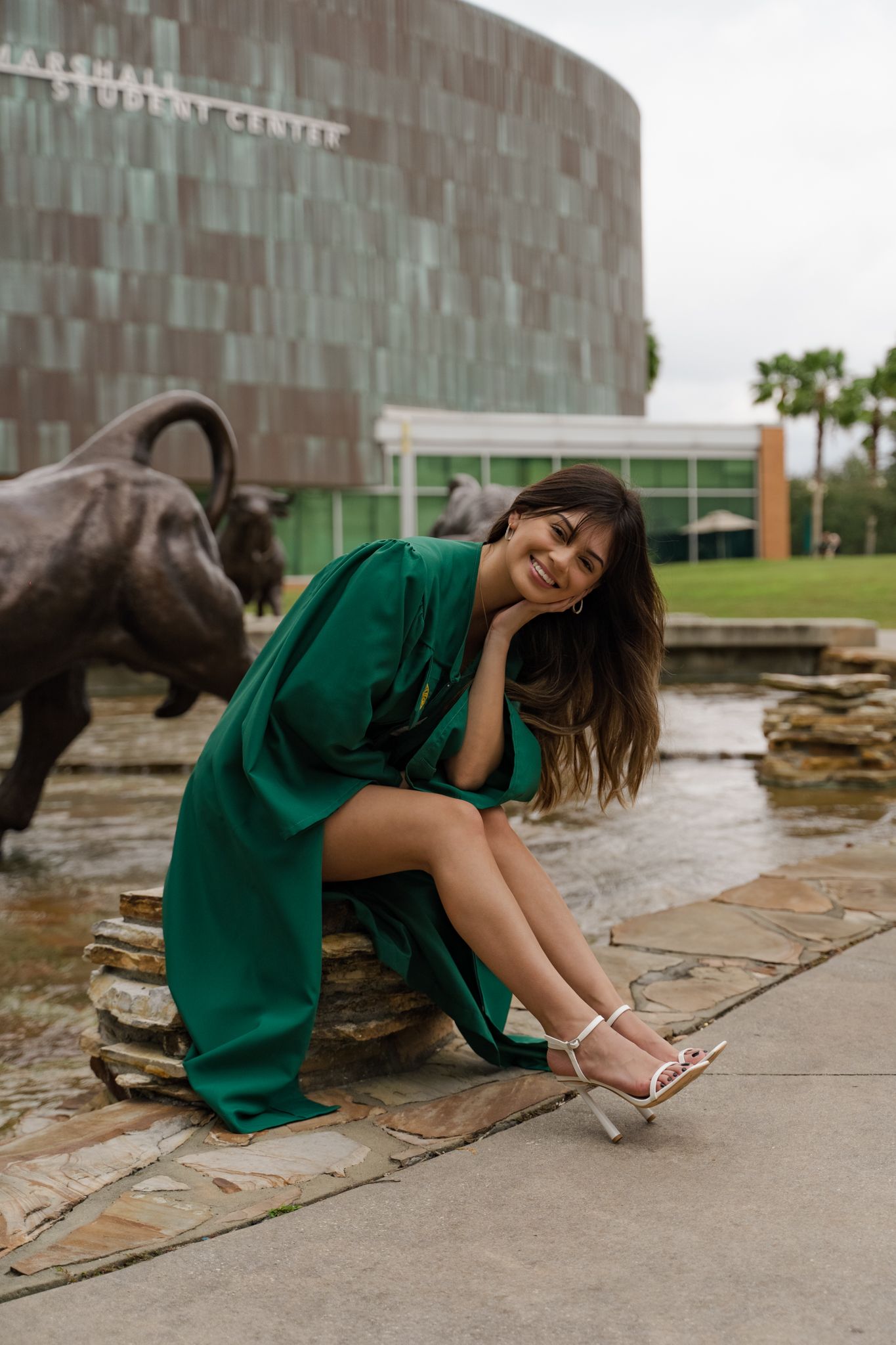 Smiling woman in green dress seated near bull fountain outside Marshall Student Center campus.